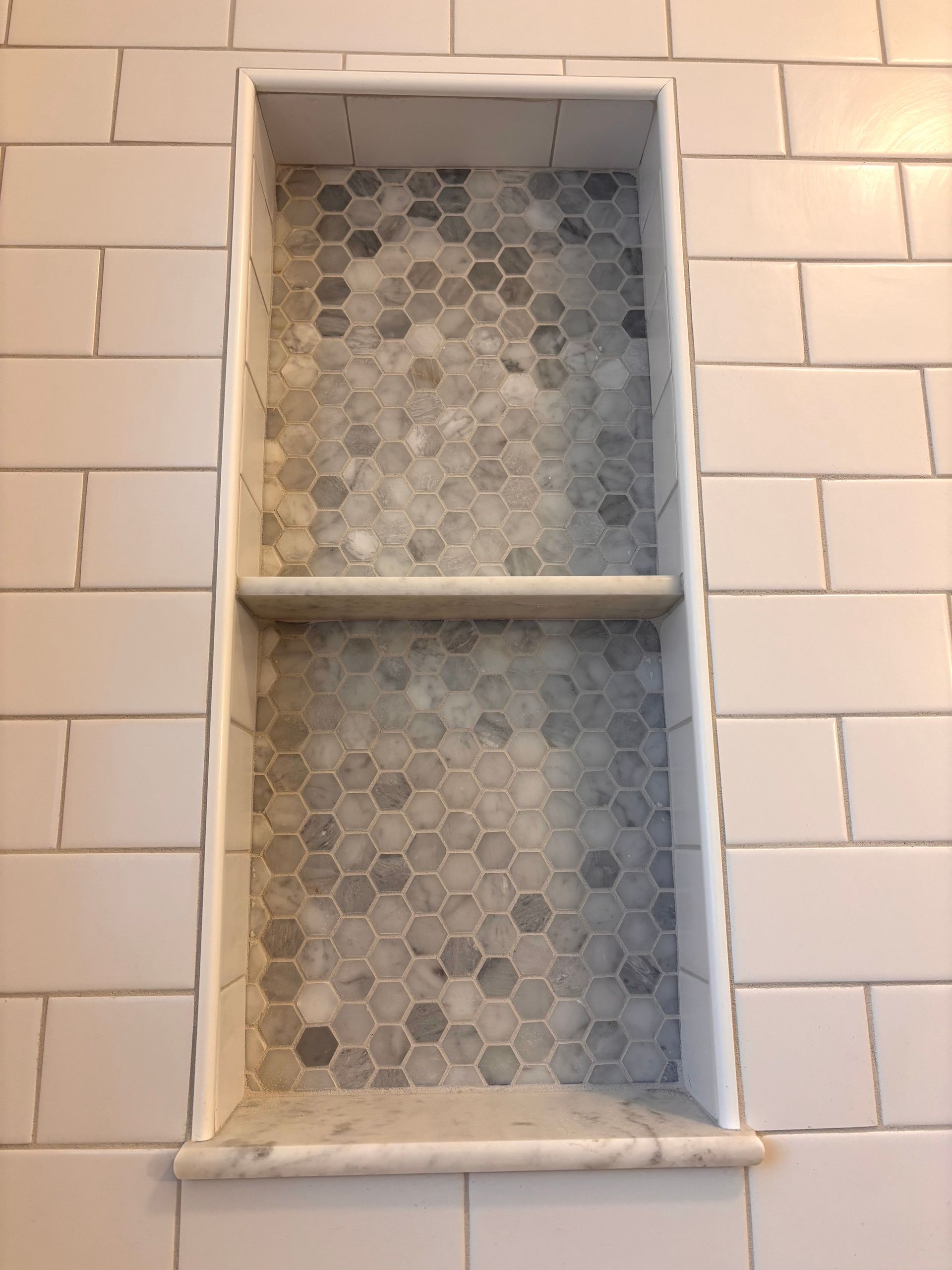 Tile shower niche with a gray hexagon tile back and white subway tile surround, with a marble shelf.