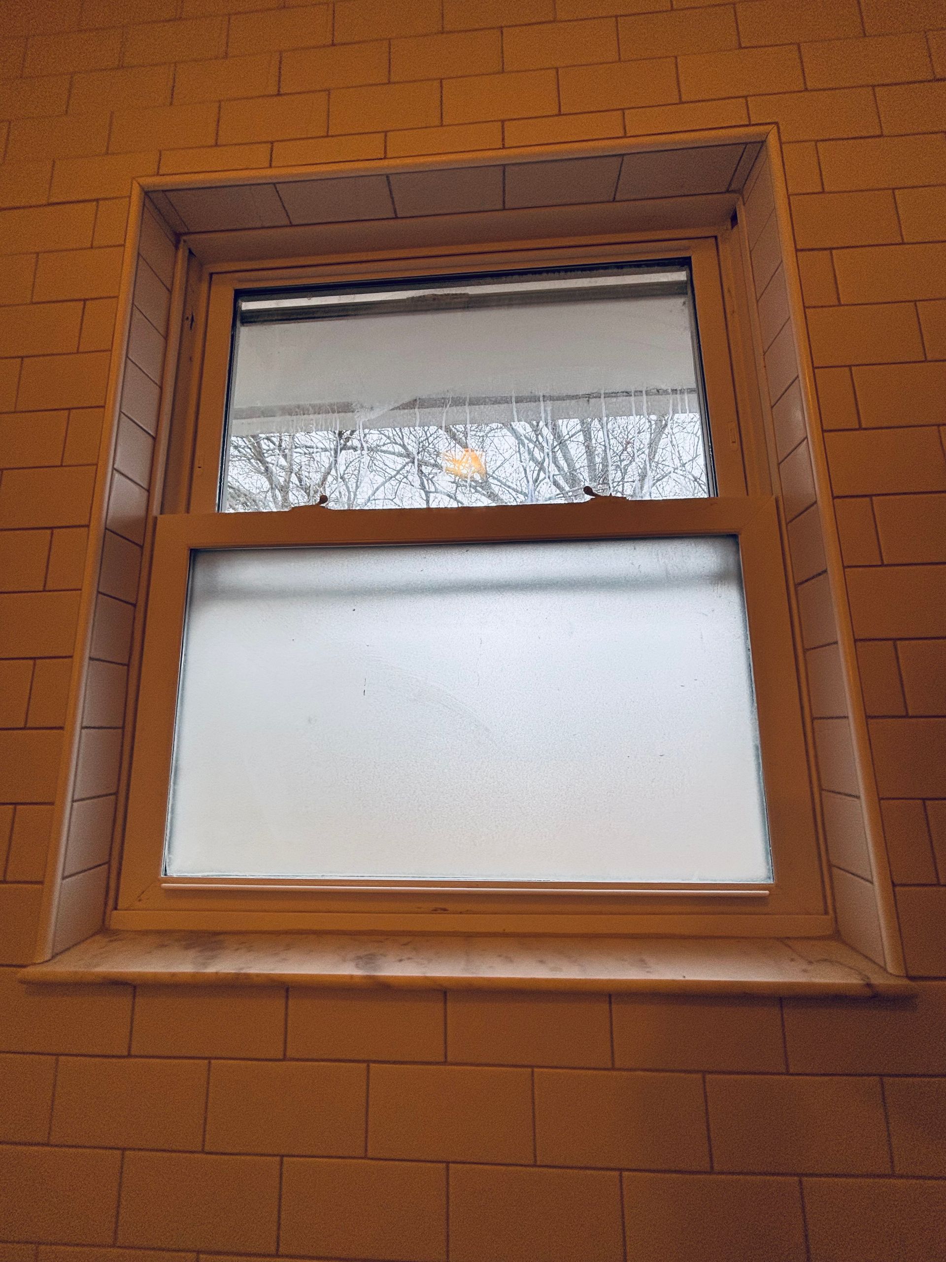 White-framed window, partially open, against a brick wall. Frosted glass in the lower pane, clear in the upper.