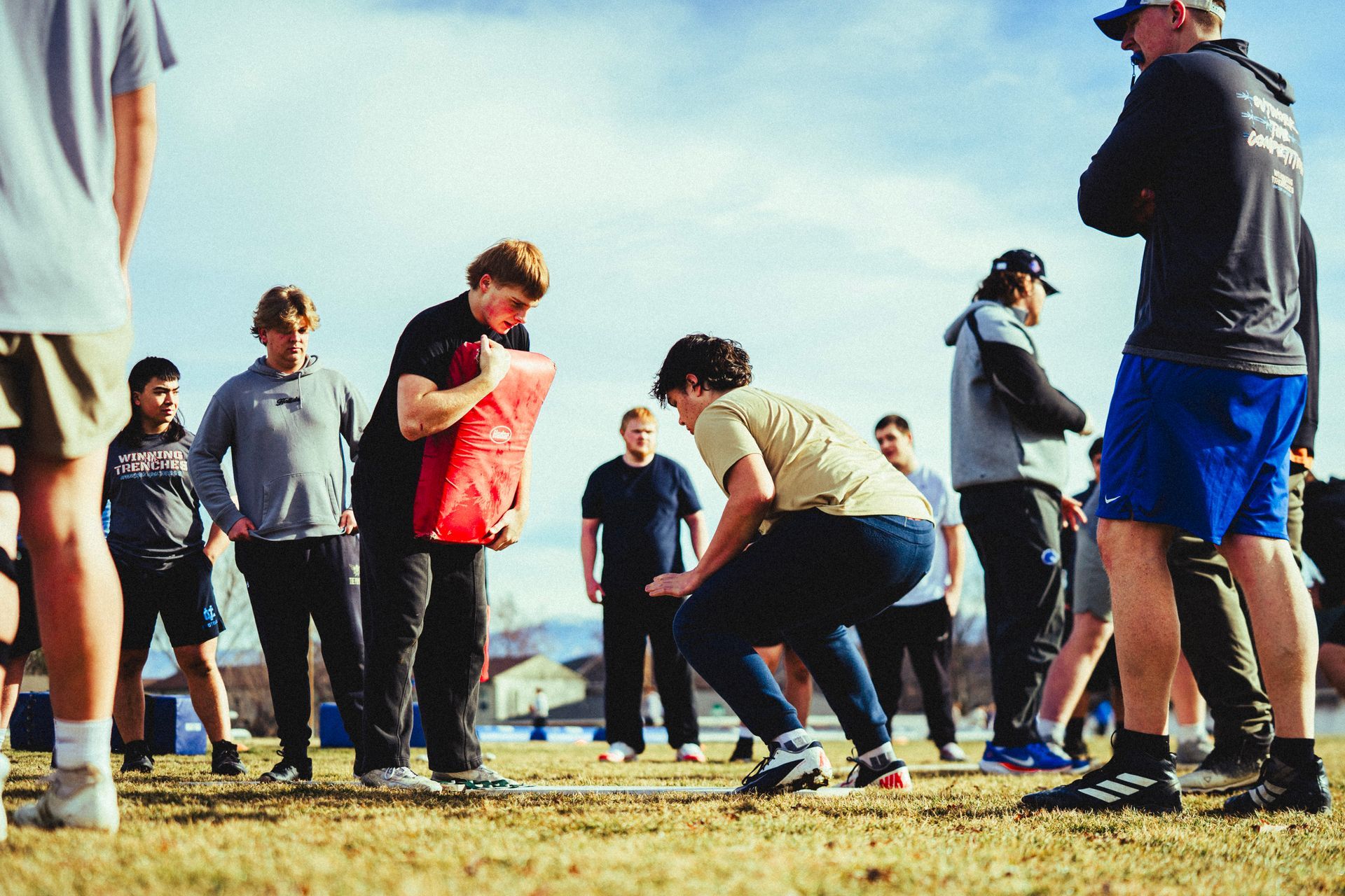 Students practicing football drills on a field with a coach supervising.