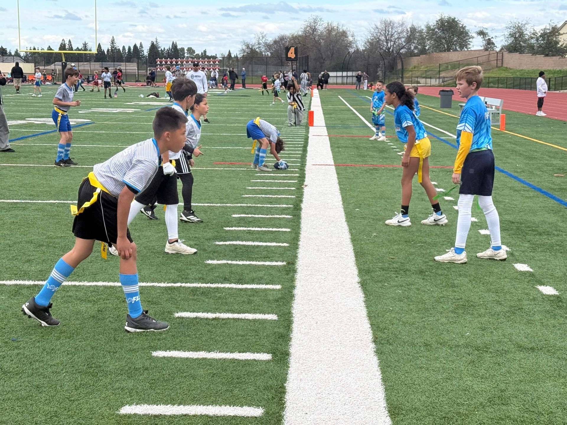 Children in sports uniforms line up on opposite sides of a marked field for a flag football game.