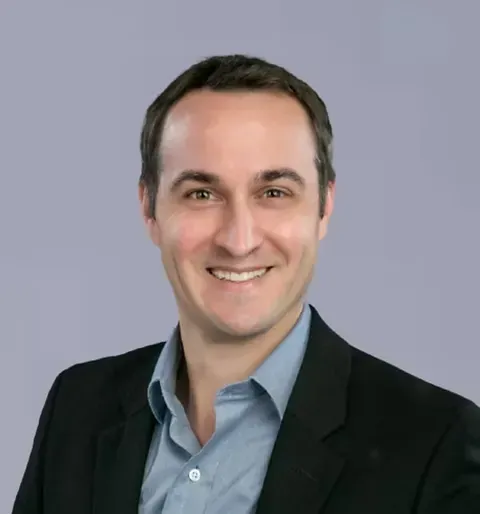 A man in a suit and blue shirt is smiling for the camera