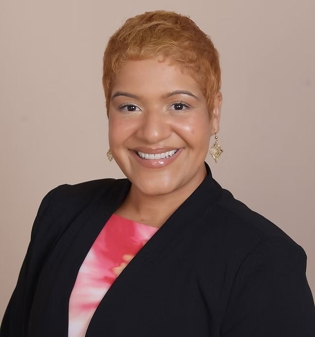 A woman wearing a black jacket and earrings smiles for the camera