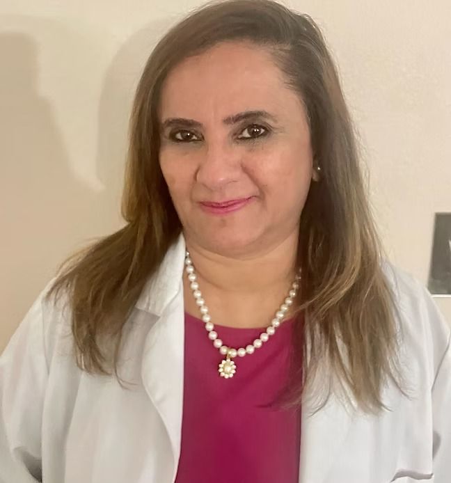 A woman in a lab coat and pearl necklace is smiling for the camera.