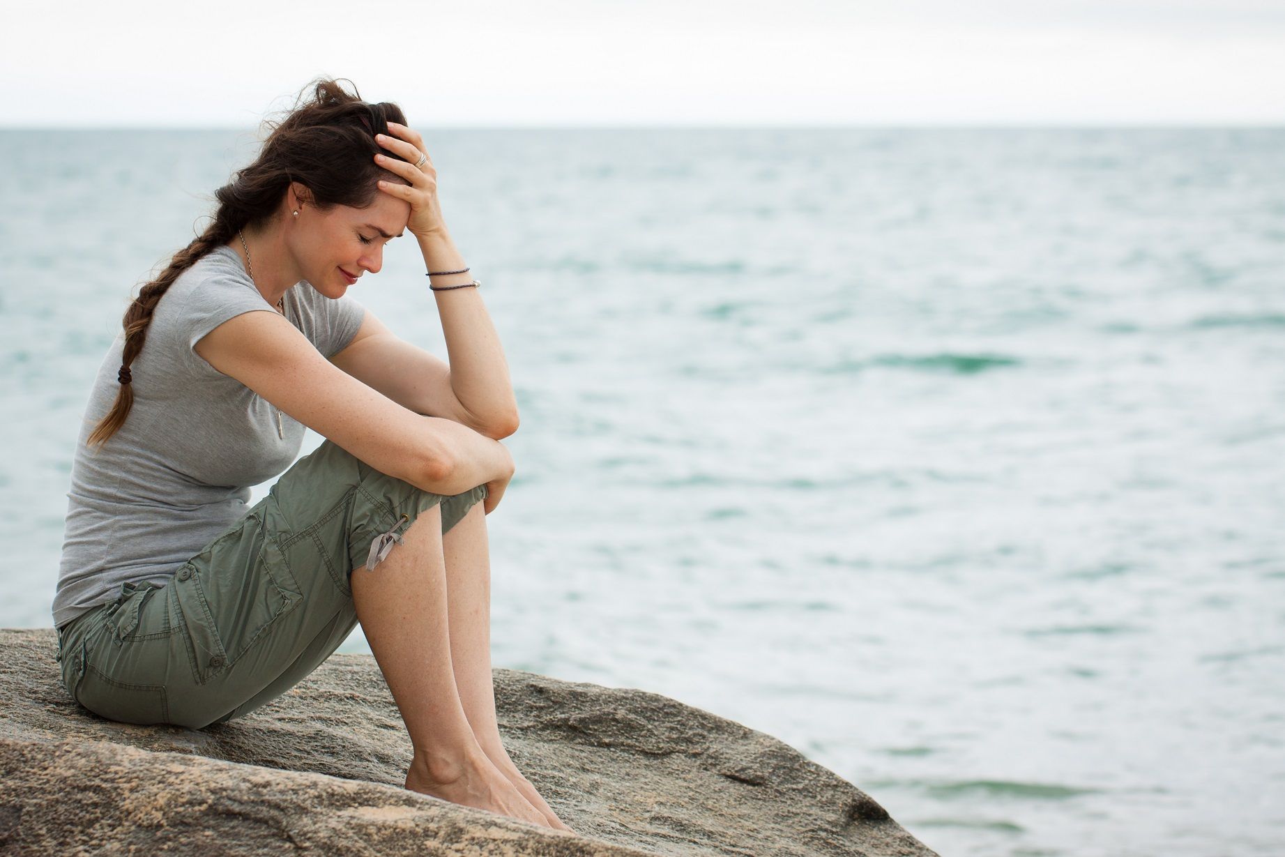 Woman sitting and crying on a rock at the beach