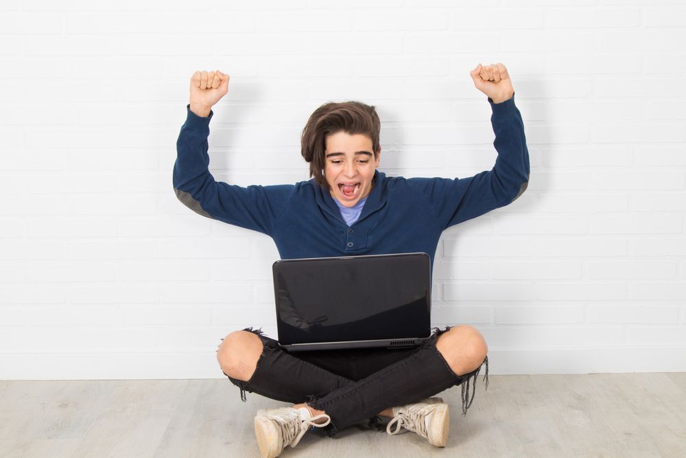 Teenager cheering while looking at a laptop computer