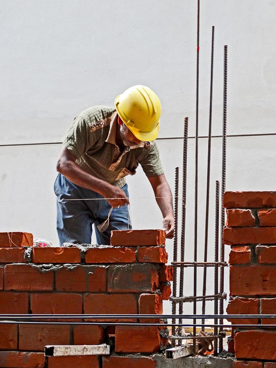 A man wearing a yellow hard hat is working on a brick wall
