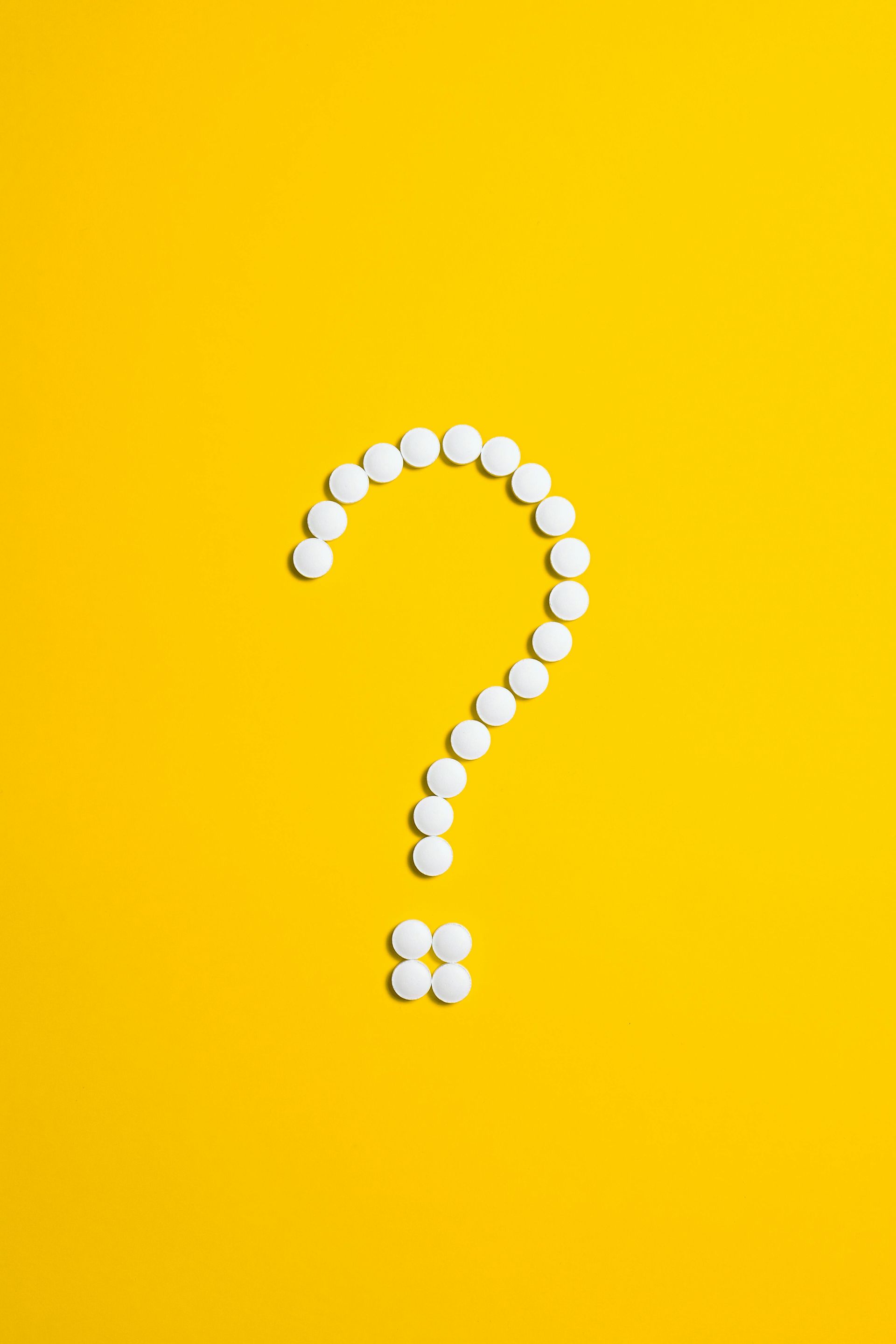 A question mark made of white pills against a bright yellow background.
