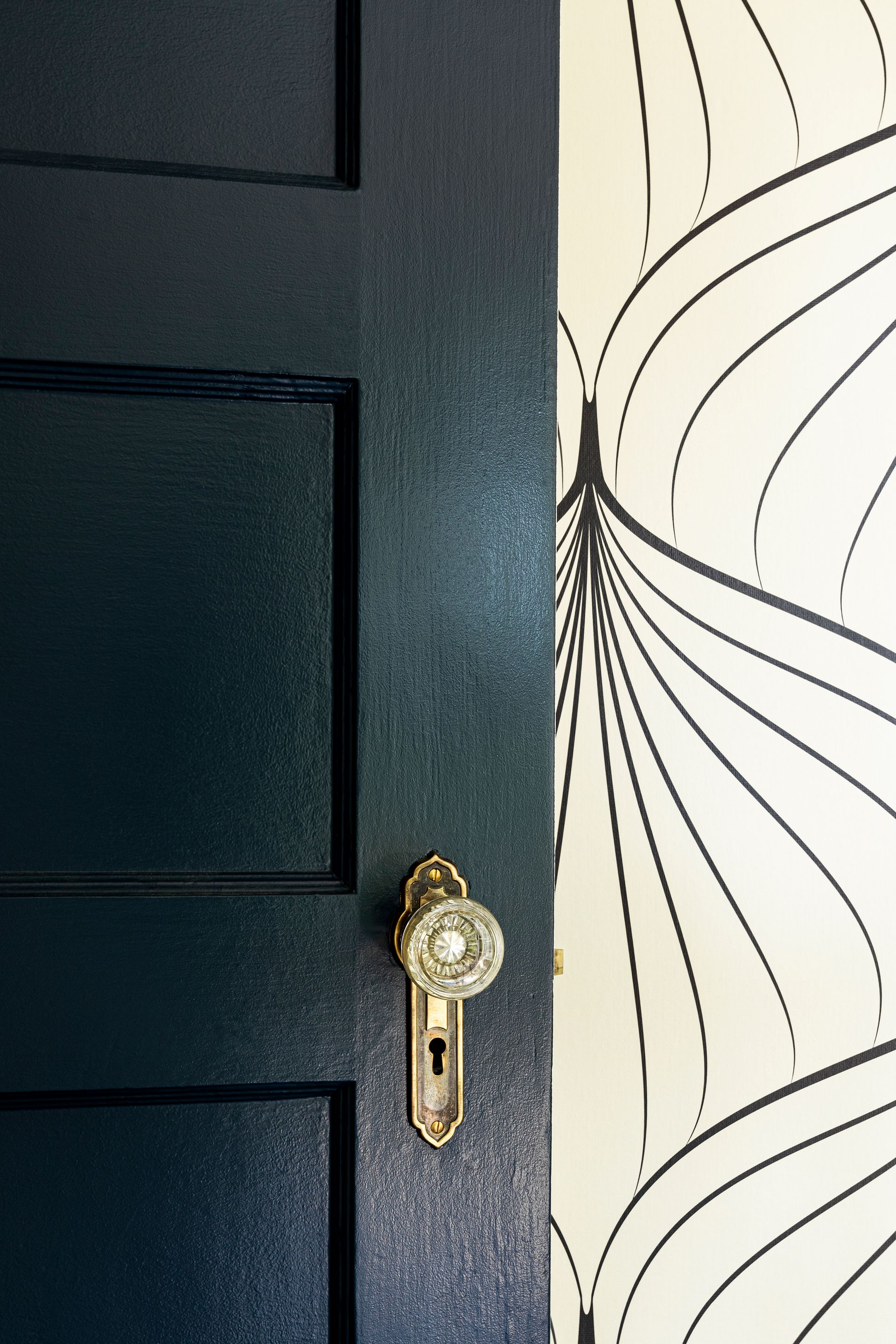 black interior door with brass hardware and graphic wallpaper detail in modern vintage bedroom