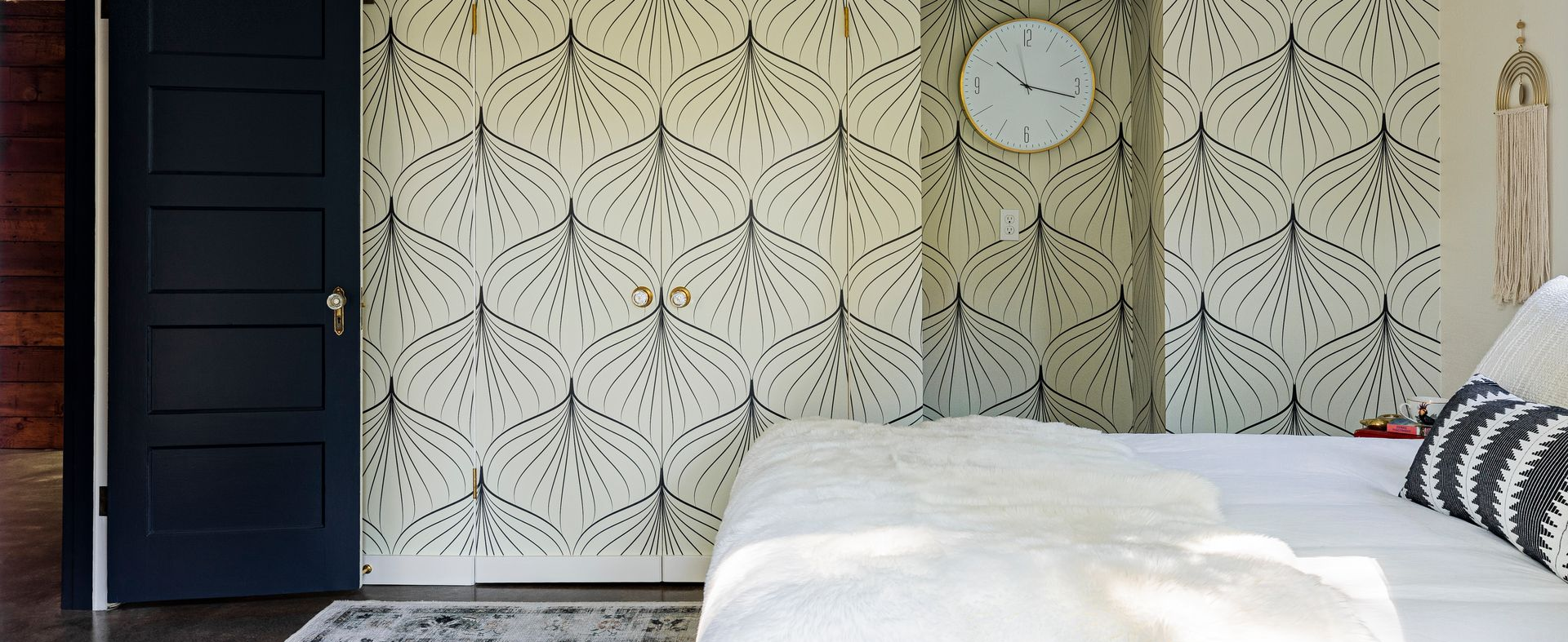 modern vintage bedroom with graphic wallpaper, black door, and neutral layered bedding