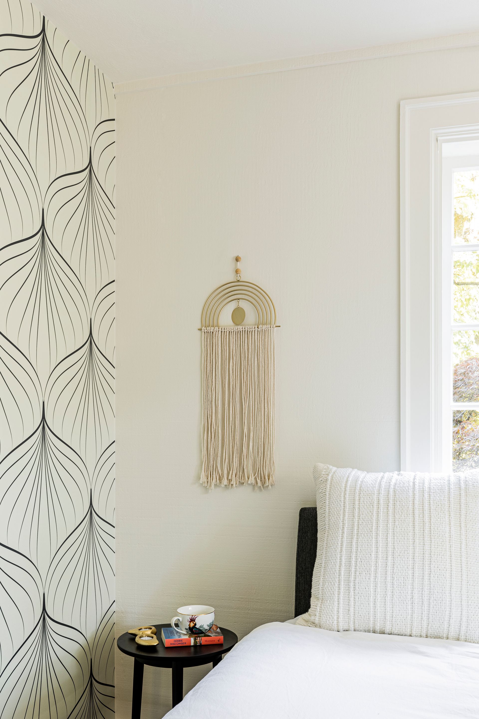 neutral bed styling with textured pillows against graphic wallpaper in modern bedroom design