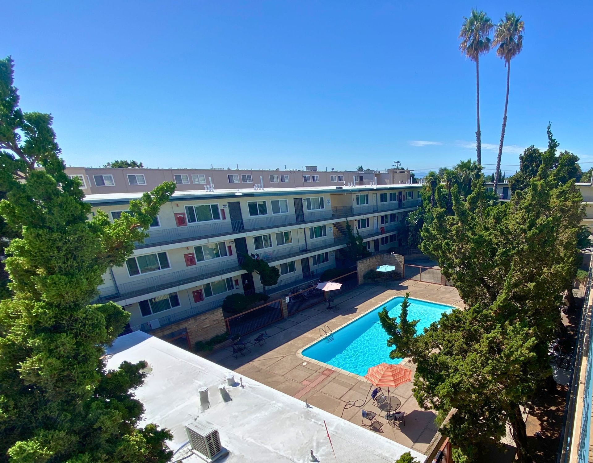 Exterior view of an apartment complex with a pool, courtyard, and palm trees.