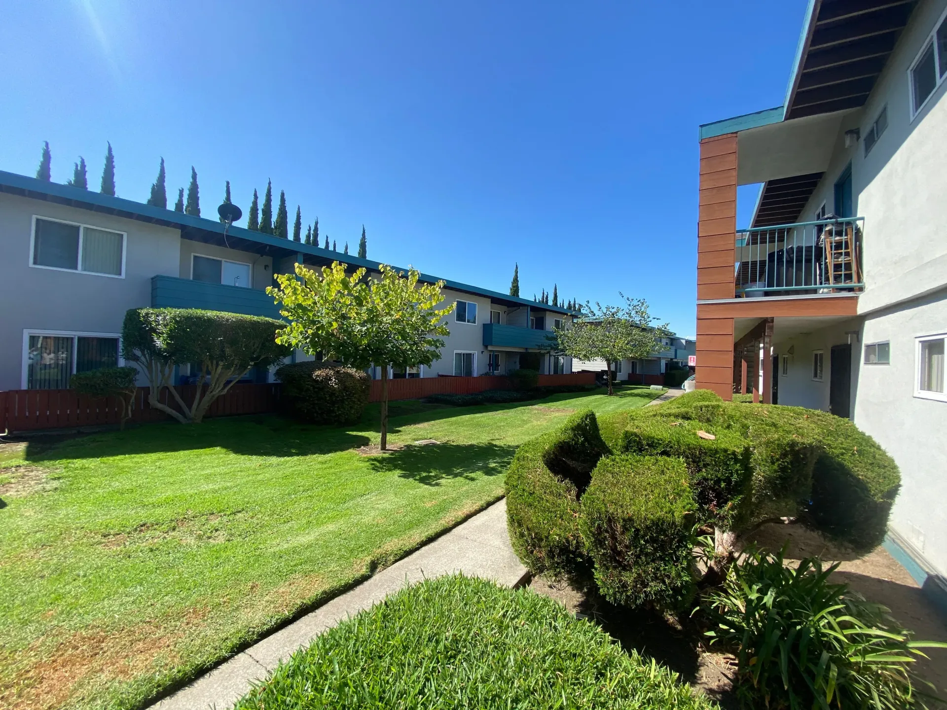 Exterior view of a garden-style apartment complex with green lawns, trees, and walkways.