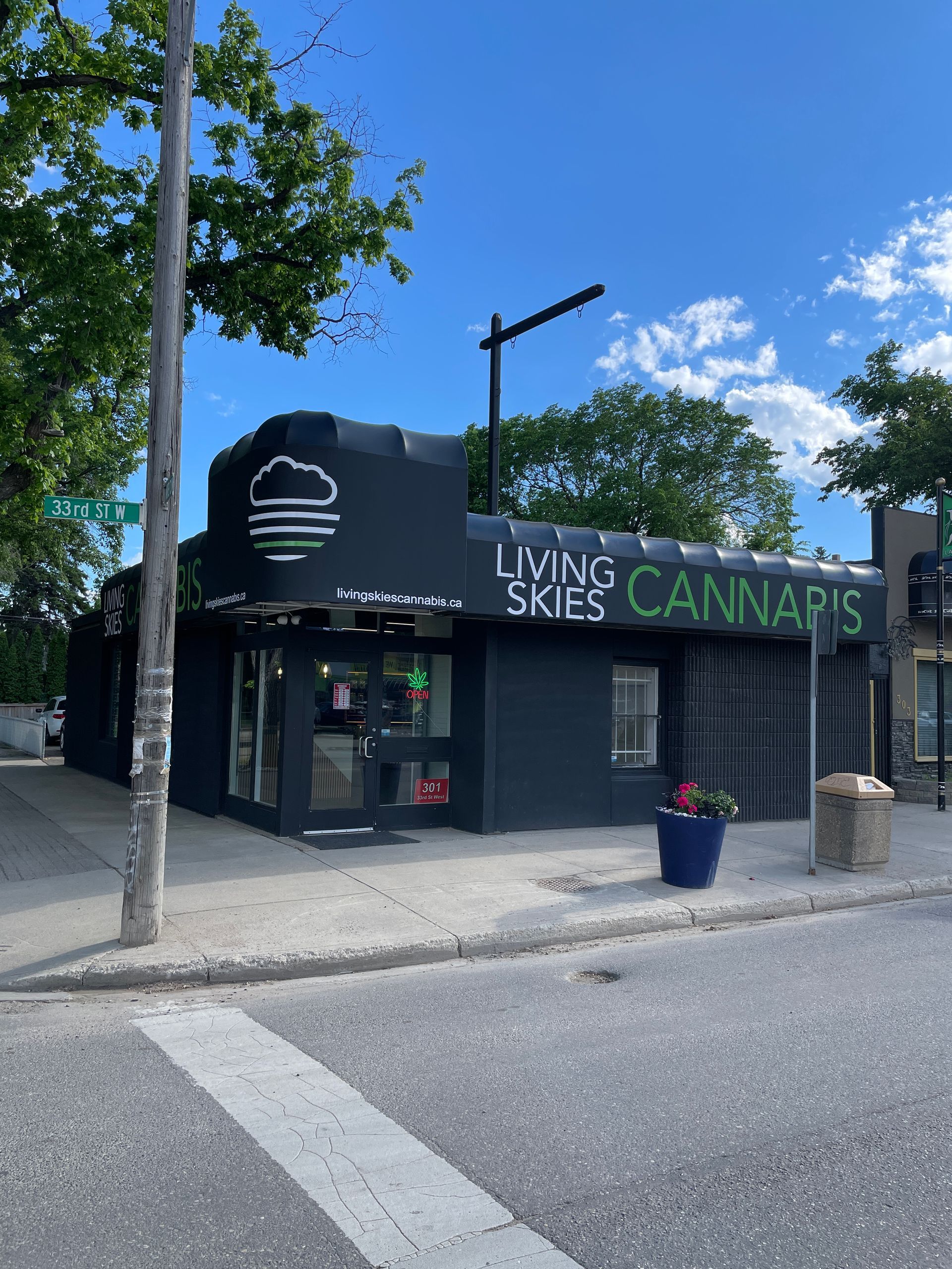 Corner cannabis dispensary on a street corner with black and green signage under a blue sky.