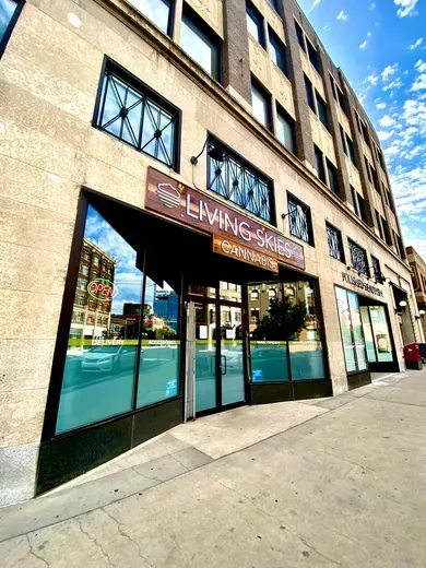 The Living Skies building exterior with glass storefronts, tan stone facade, and a blue sky in a city setting.