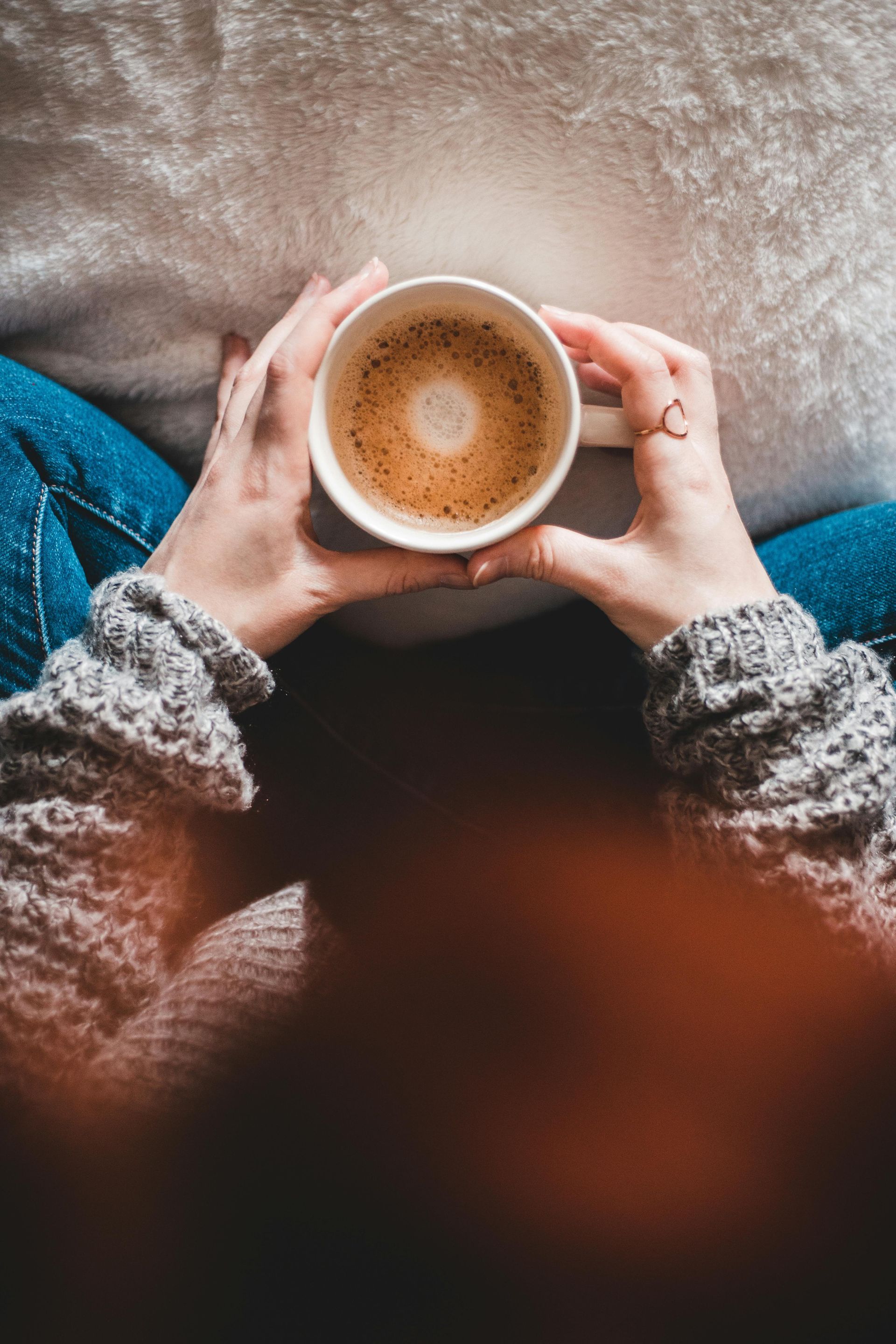 Hands holding a white mug of coffee on a cozy sweater and blanket background