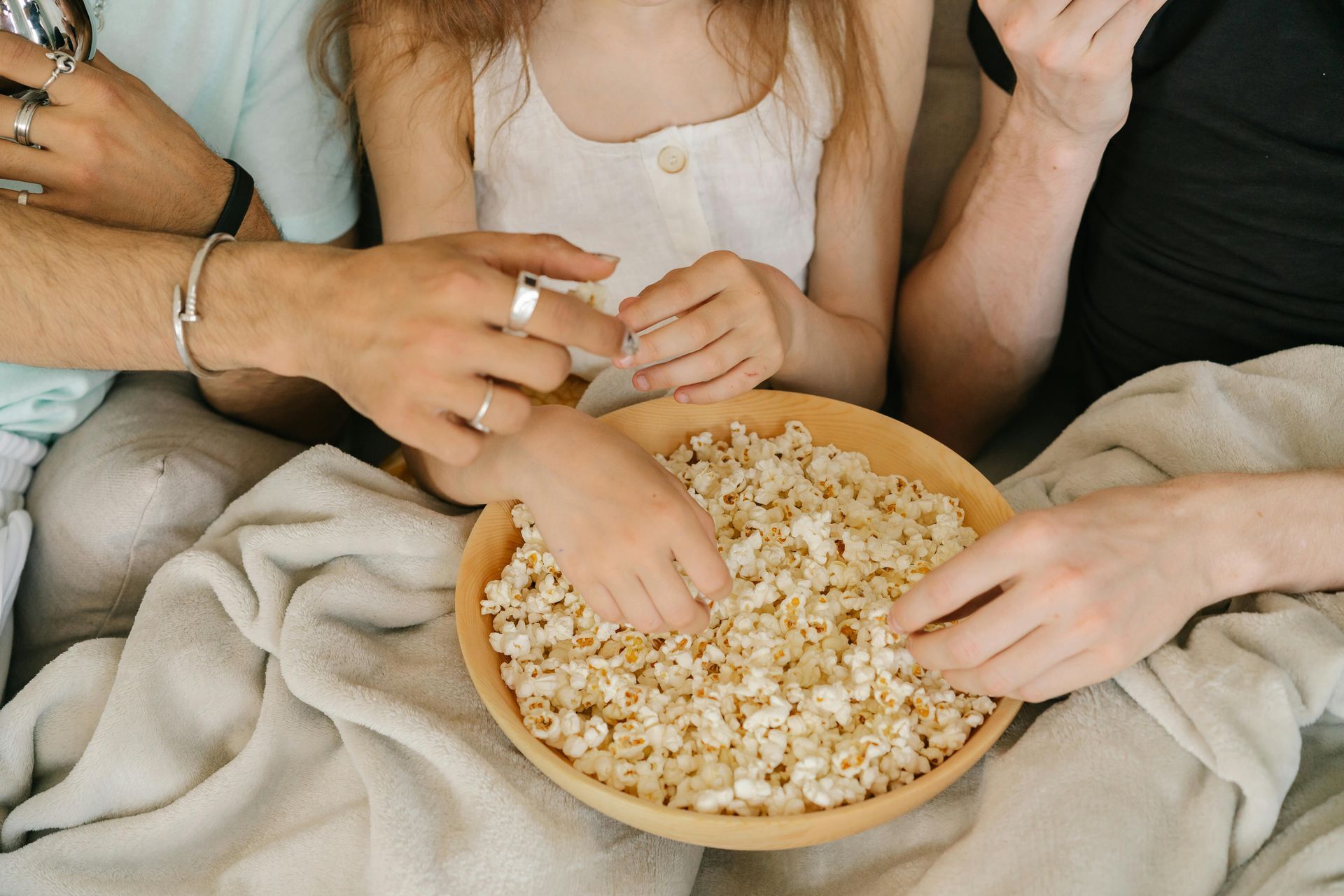 Several hands reaching for popcorn in a bowl on a blanket during a cozy gathering