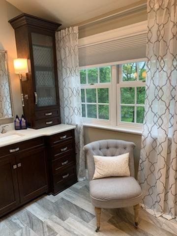 A bathroom with a chair , sink , mirror and window.