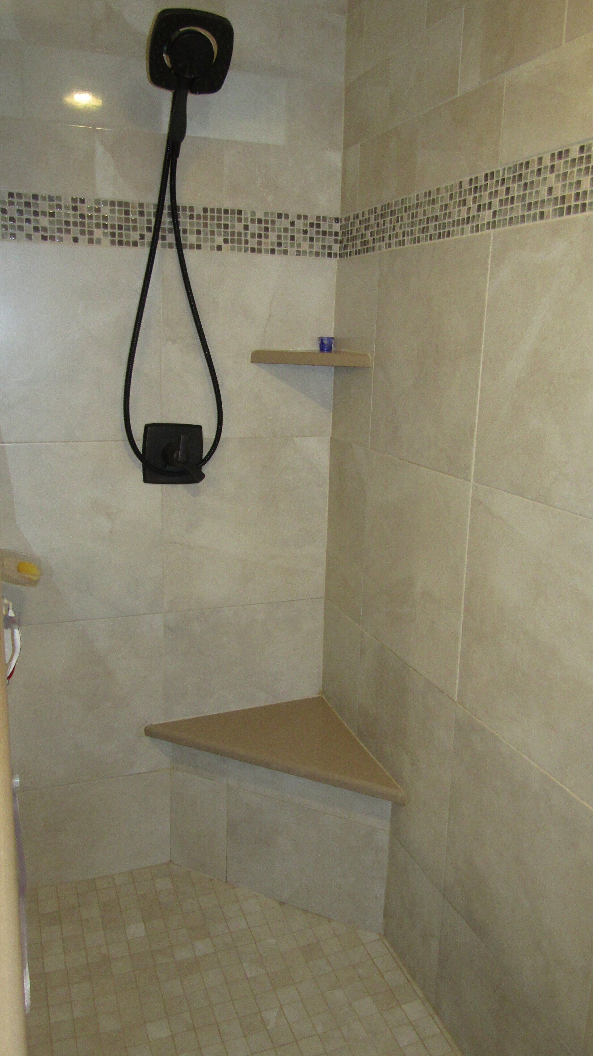 A shower with a corner seat and a shower head.