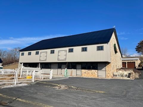 A large barn with a black roof is sitting on top of a hill.