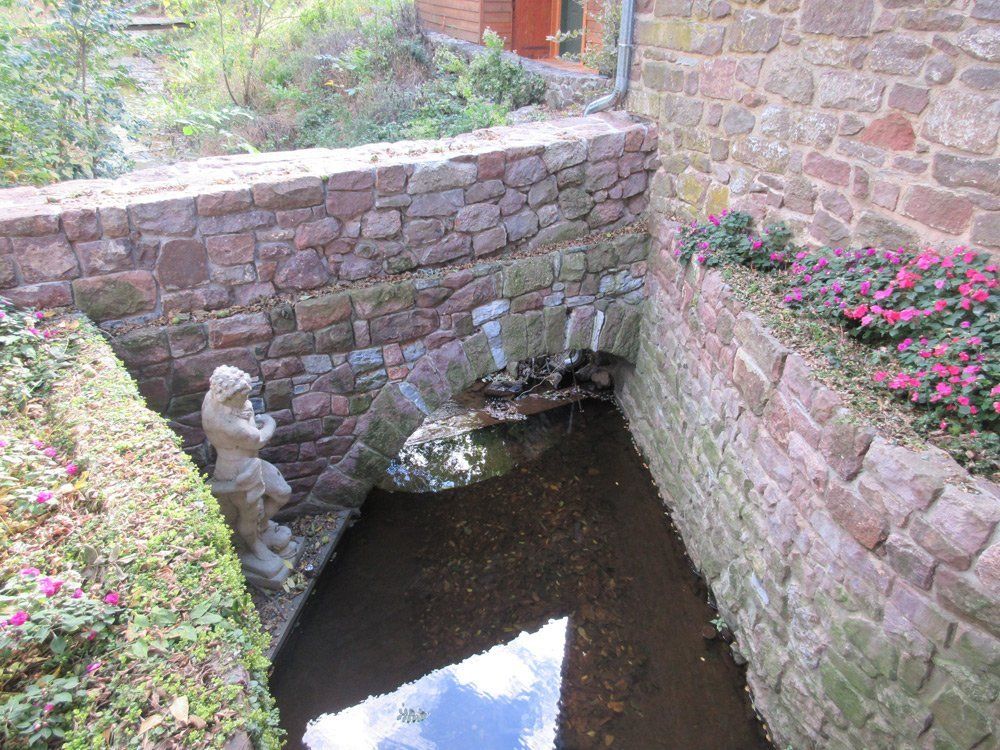 A stone wall surrounds a pond with a statue in the middle of it.