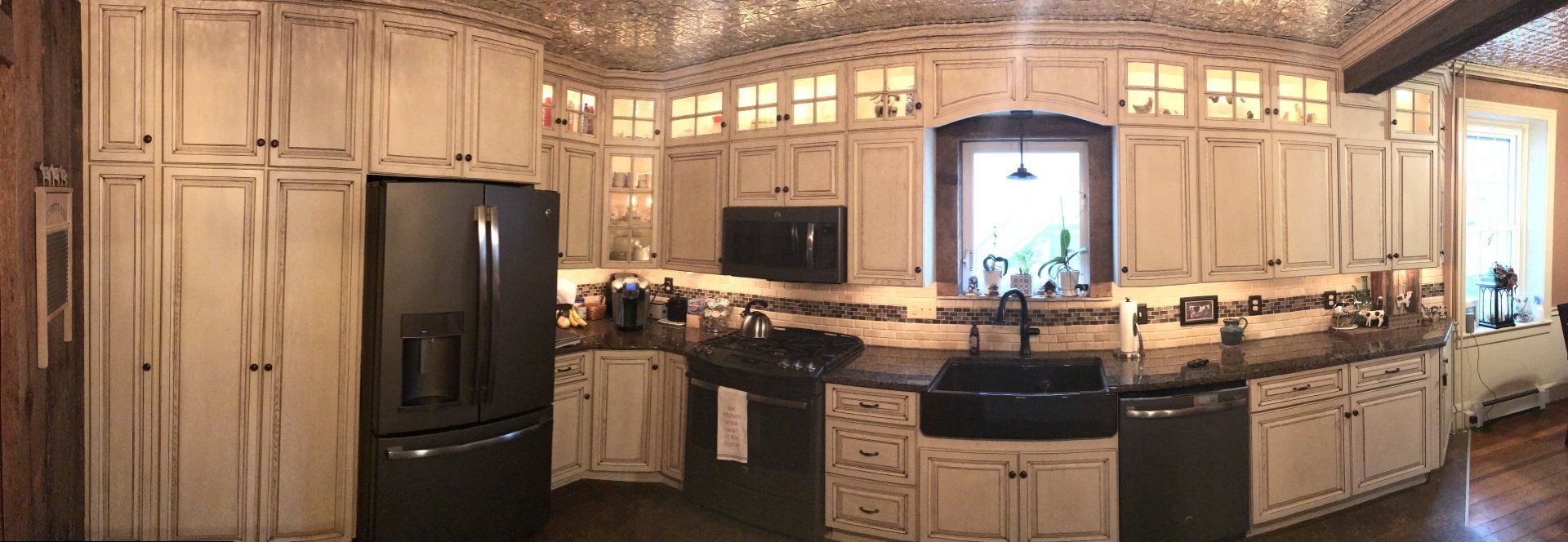 A kitchen with white cabinets , black appliances , a sink , a refrigerator , and a window.