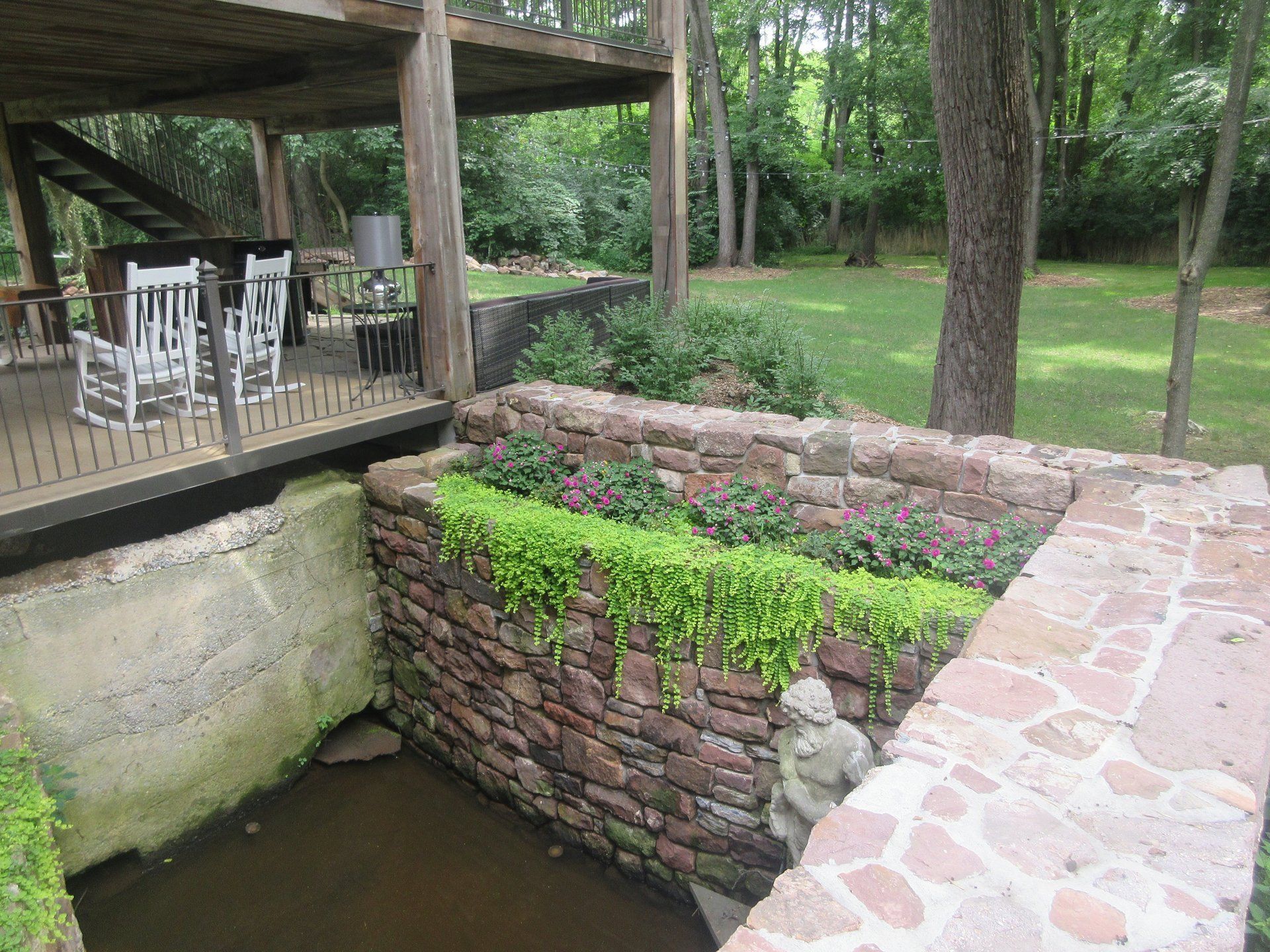 A stone wall surrounds a pond with a statue in the middle of it.