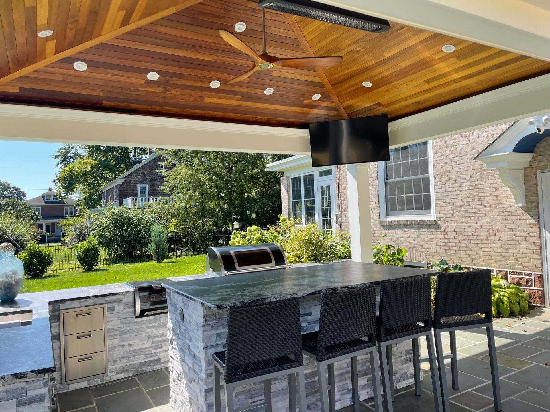 A patio with a table , chairs , a grill and a ceiling fan.