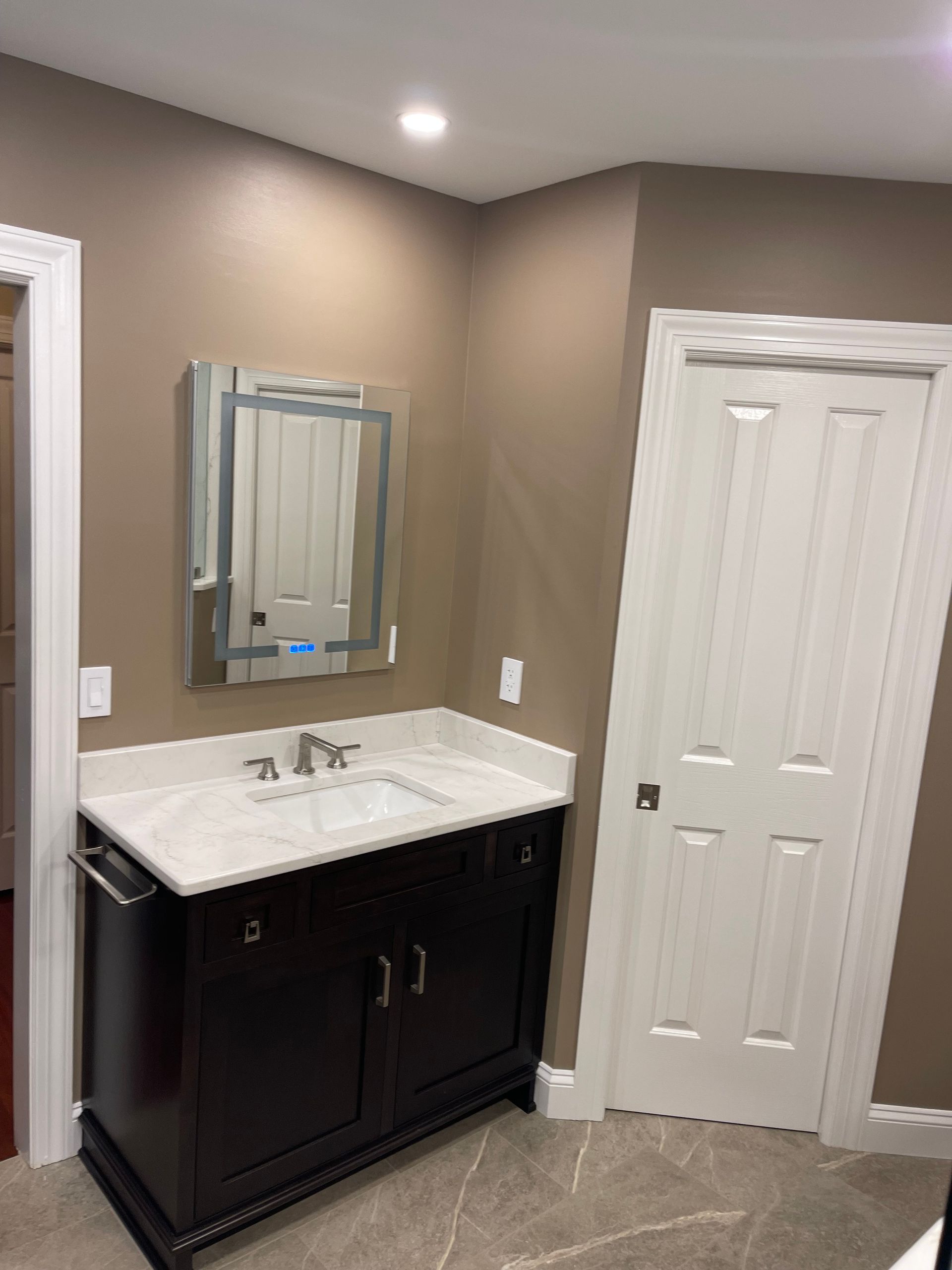 A bathroom with a sink , mirror and door.