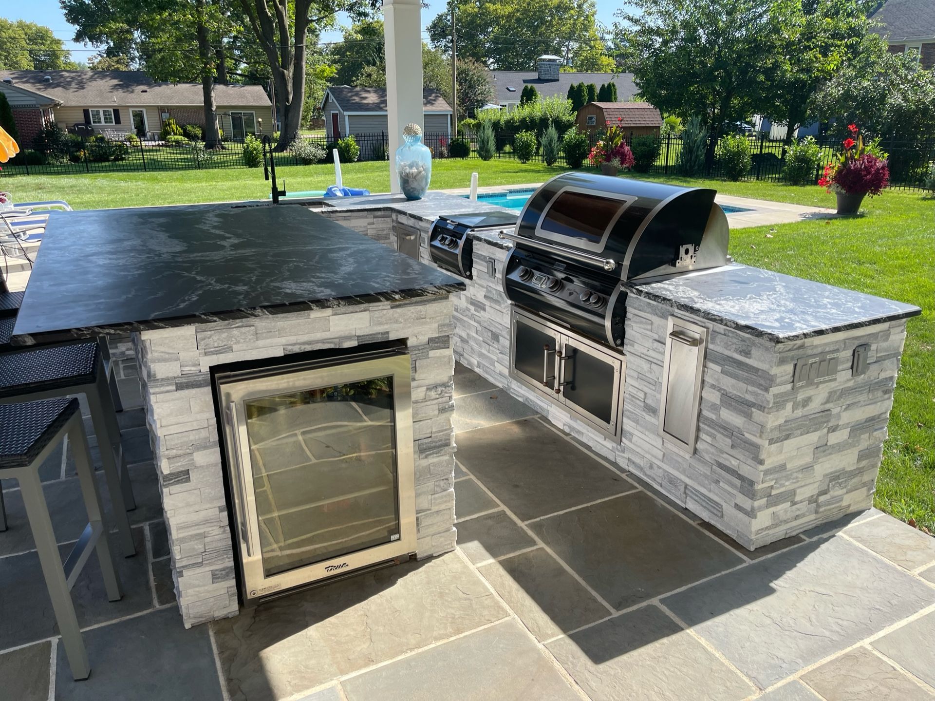 A large outdoor kitchen with a grill and a refrigerator.