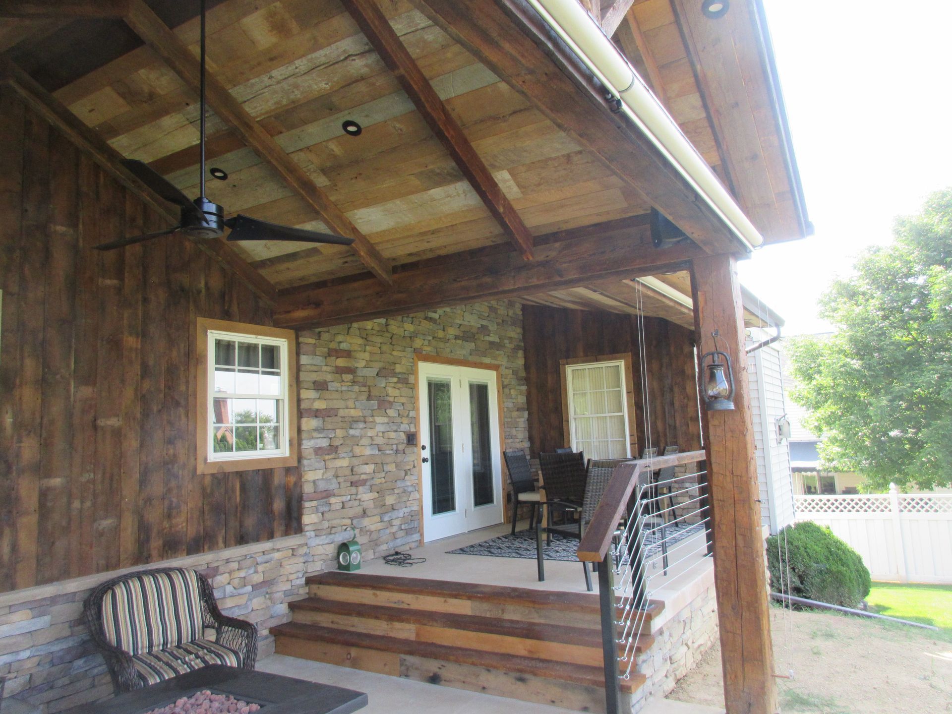 There is a porch with a ceiling fan and a bench.