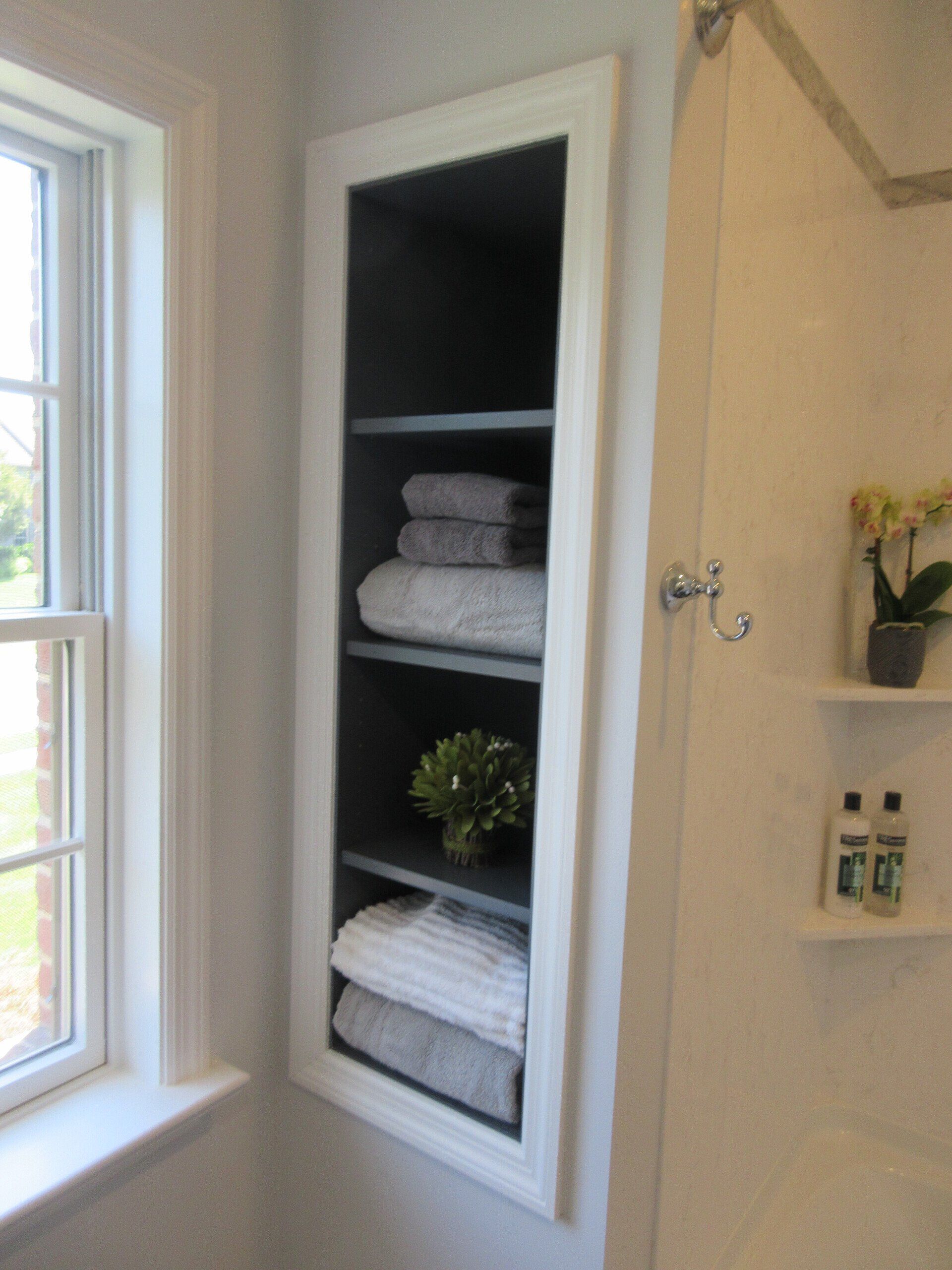 A bathroom with a window and a shelf with towels on it