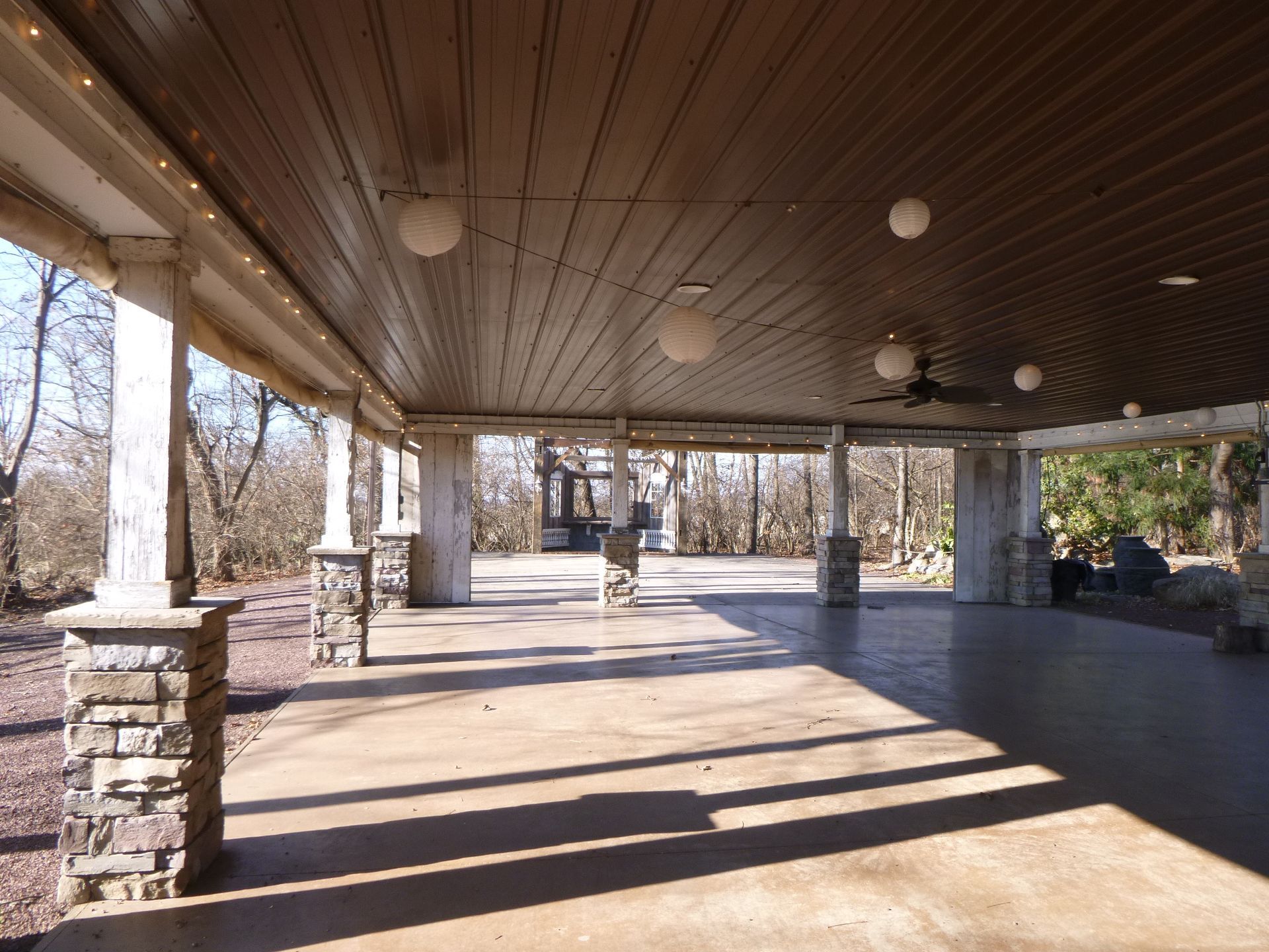 A large covered area with a ceiling fan and trees in the background
