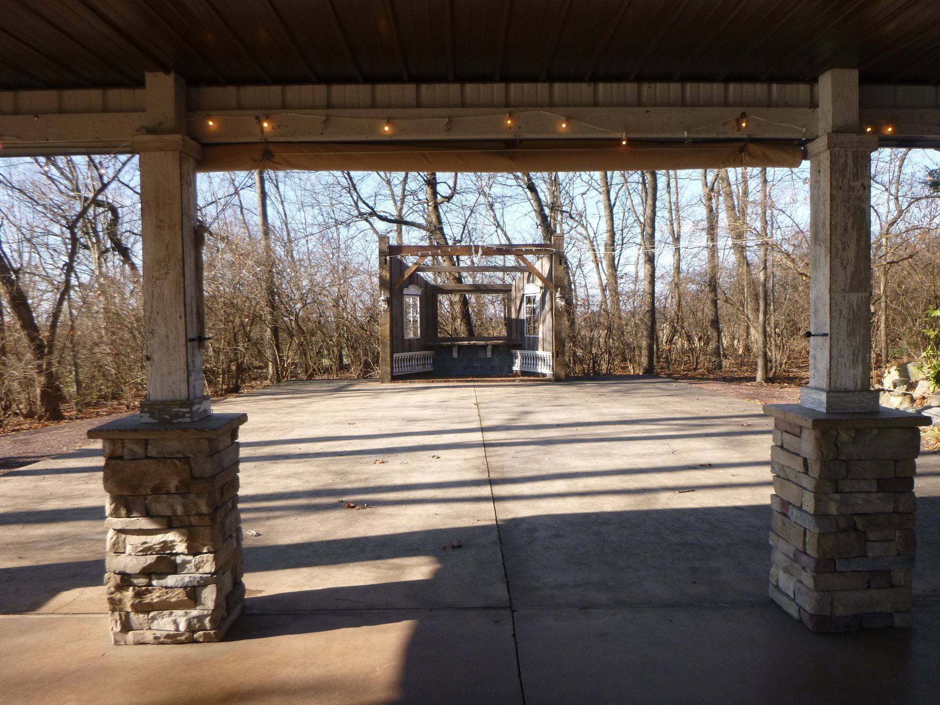 An empty pavilion with a gazebo in the background and trees in the background.