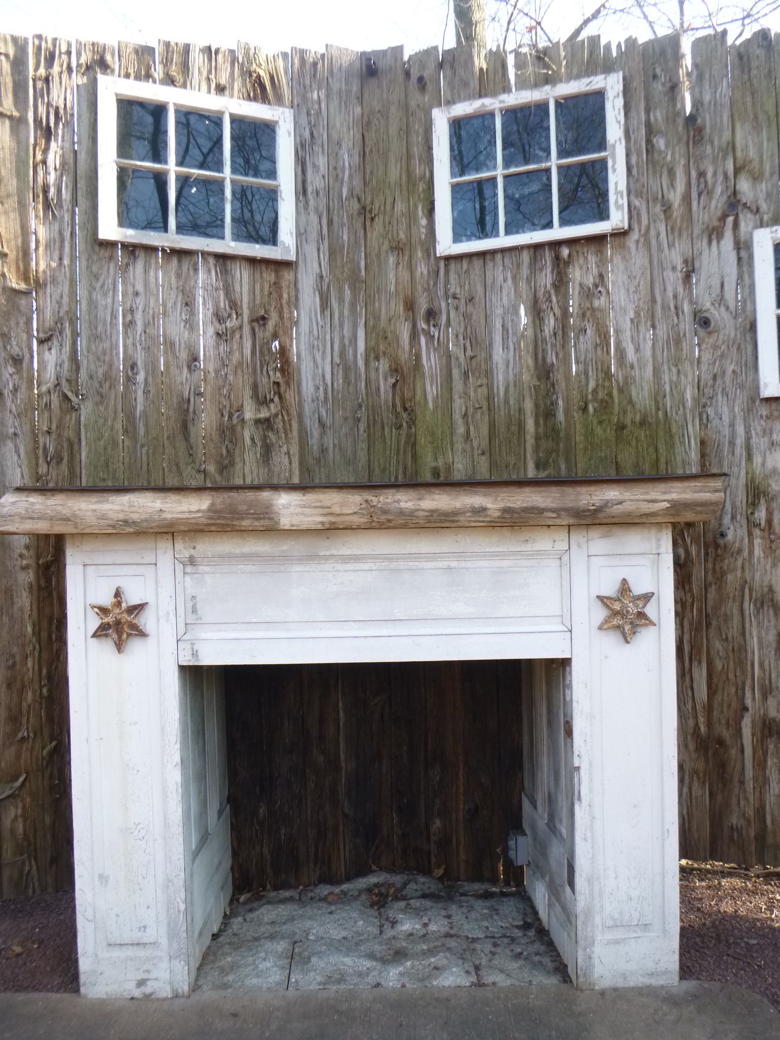 A white fireplace in front of a wooden wall with two windows