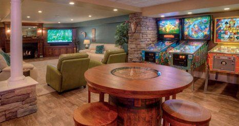 A basement with a table , chairs , and pinball machines.