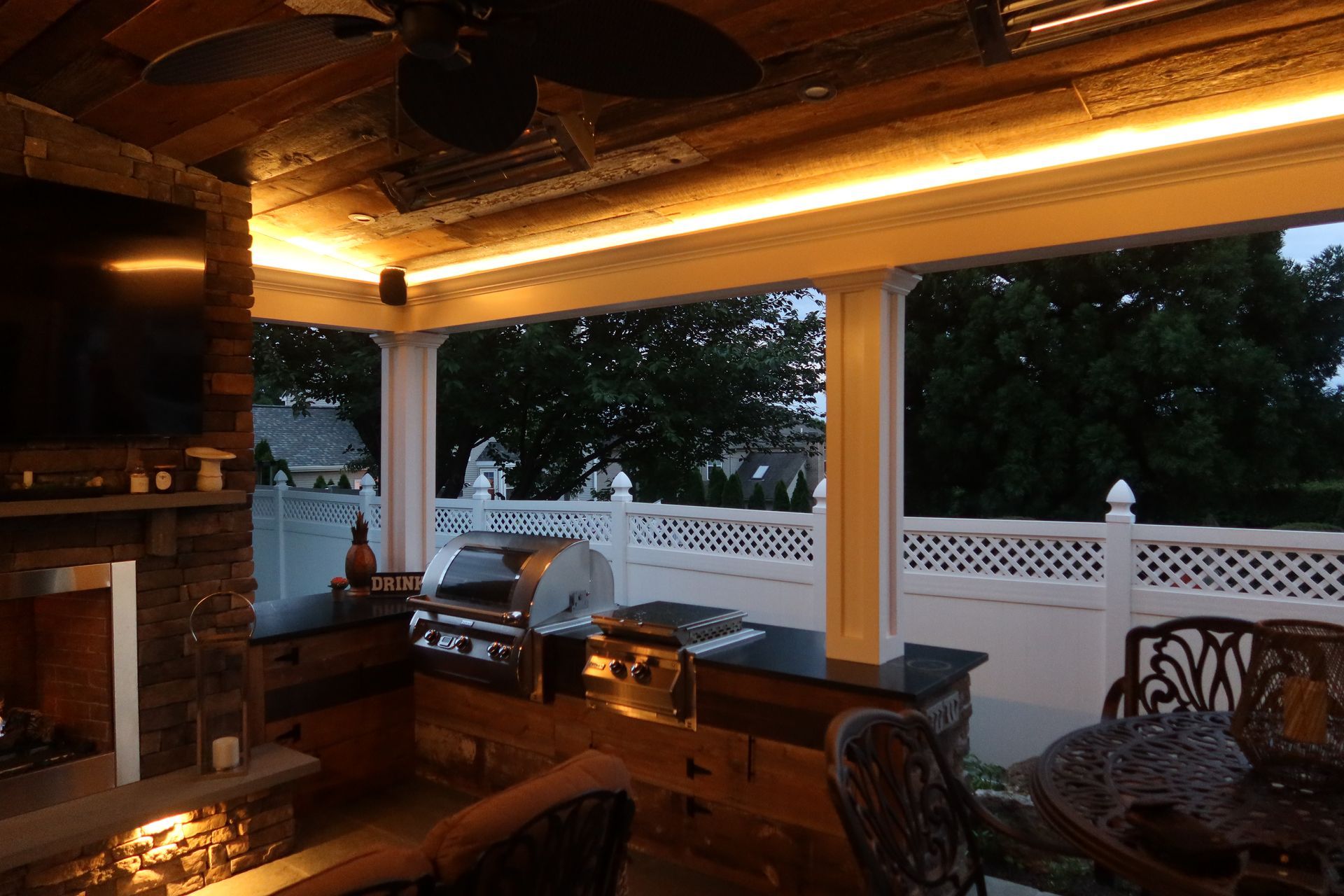 A patio with a grill , table , chairs and a television.