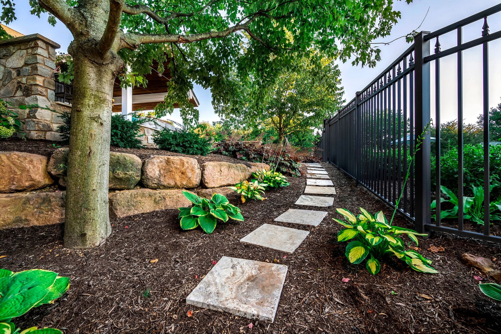 A stone walkway leading to a house with a fence and a tree.