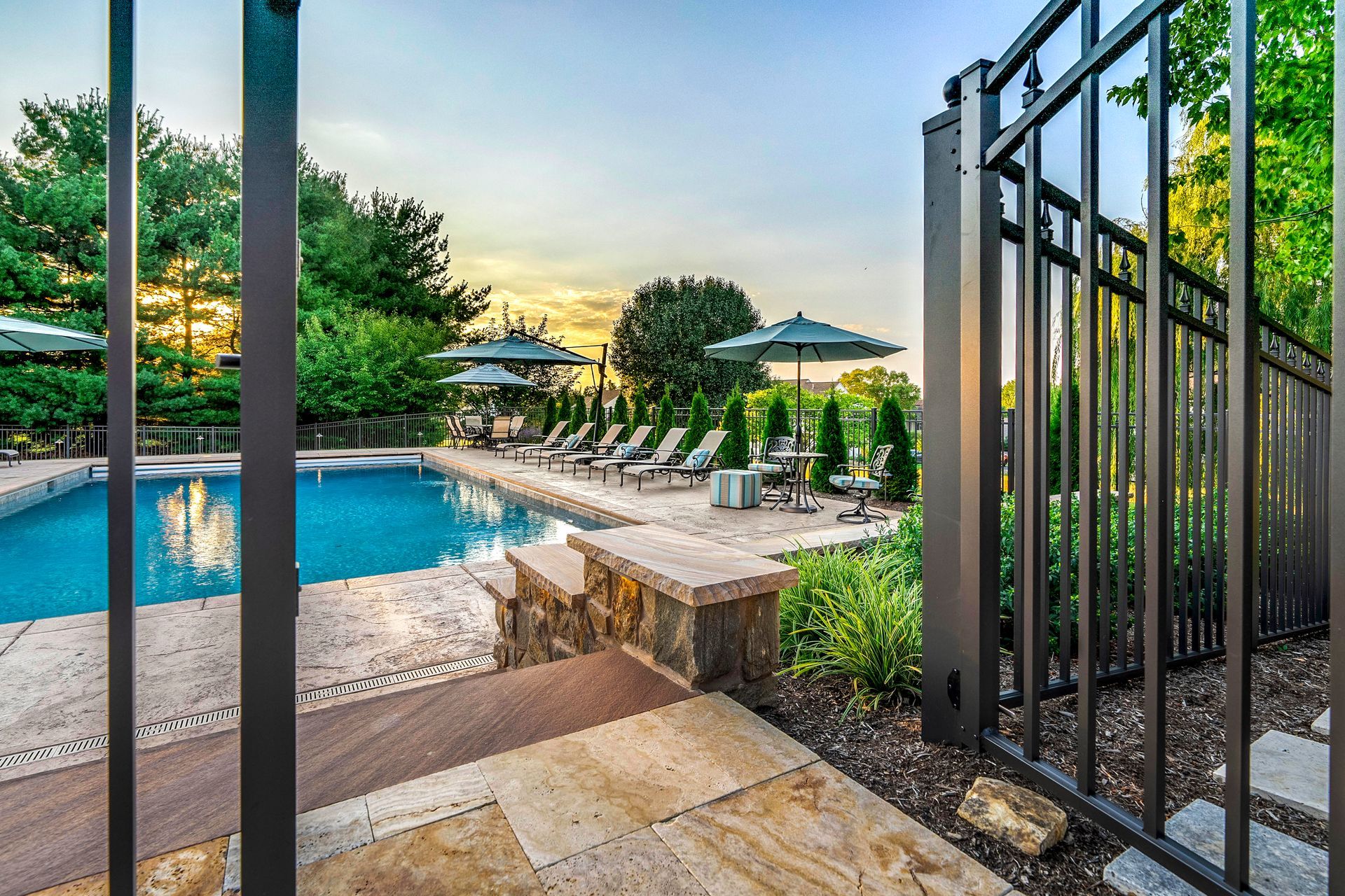 A fence surrounds a large swimming pool with chairs and umbrellas.
