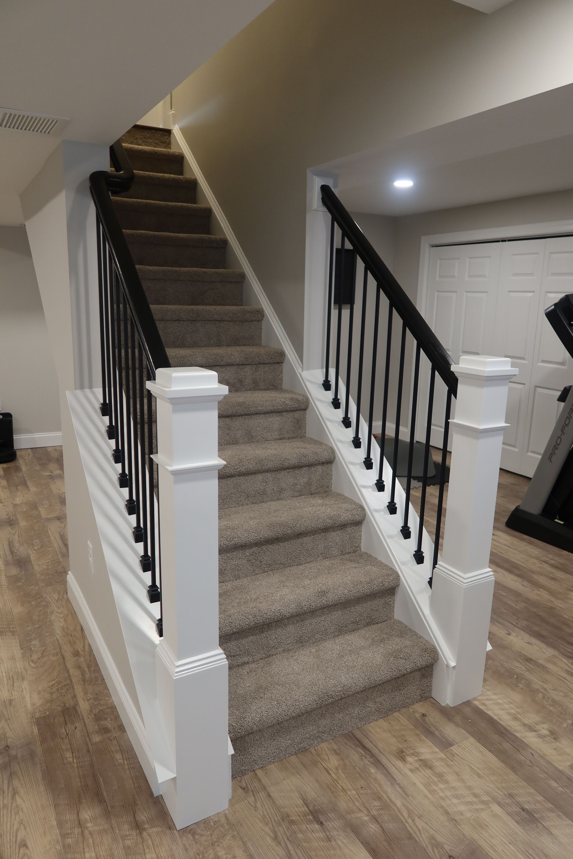 A staircase with carpeted steps and a black railing in a basement.