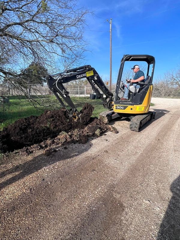 A man is driving a small excavator on a gravel road.