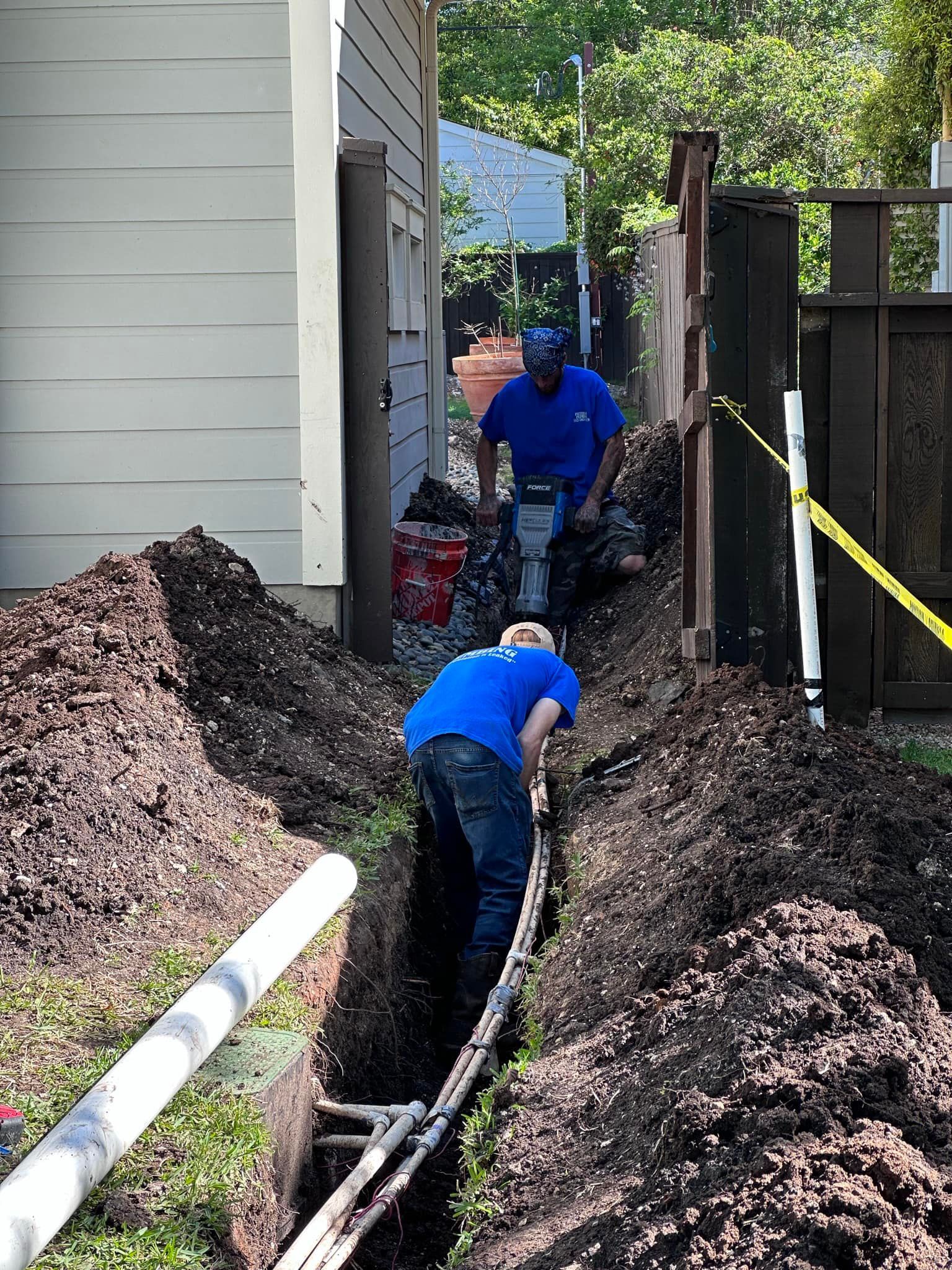 Two men are digging a hole in the ground in front of a house.