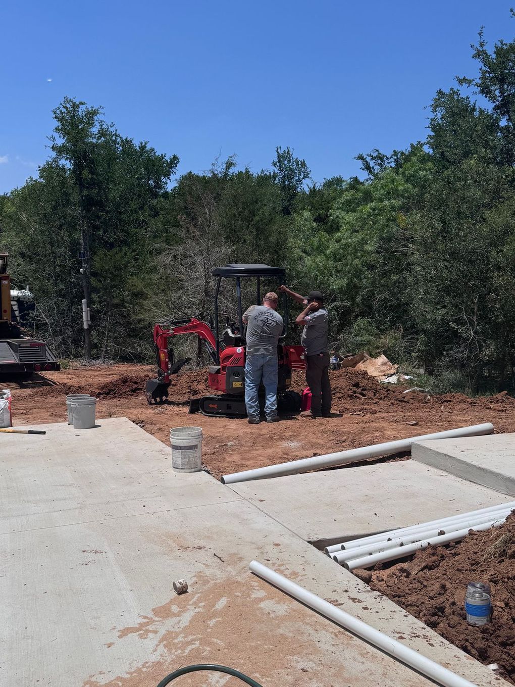 A group of men are standing next to a red excavator in a dirt field.