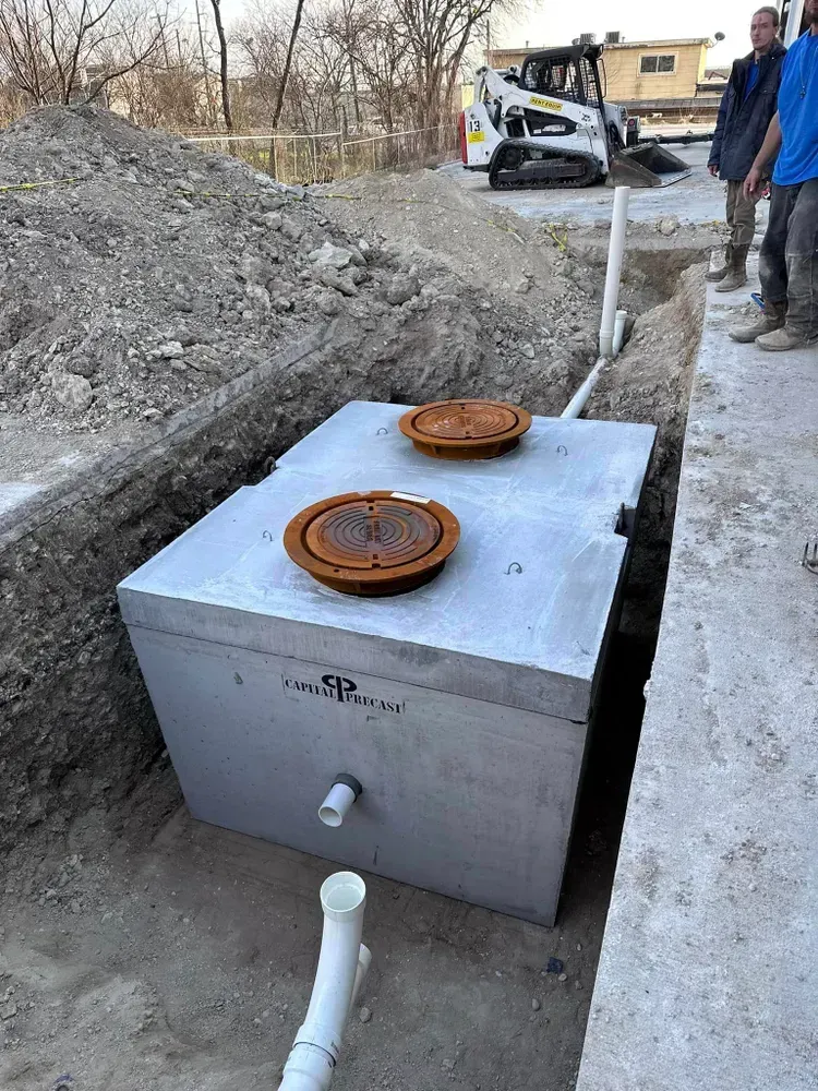 A concrete septic tank is being installed in a trench next to a bulldozer.