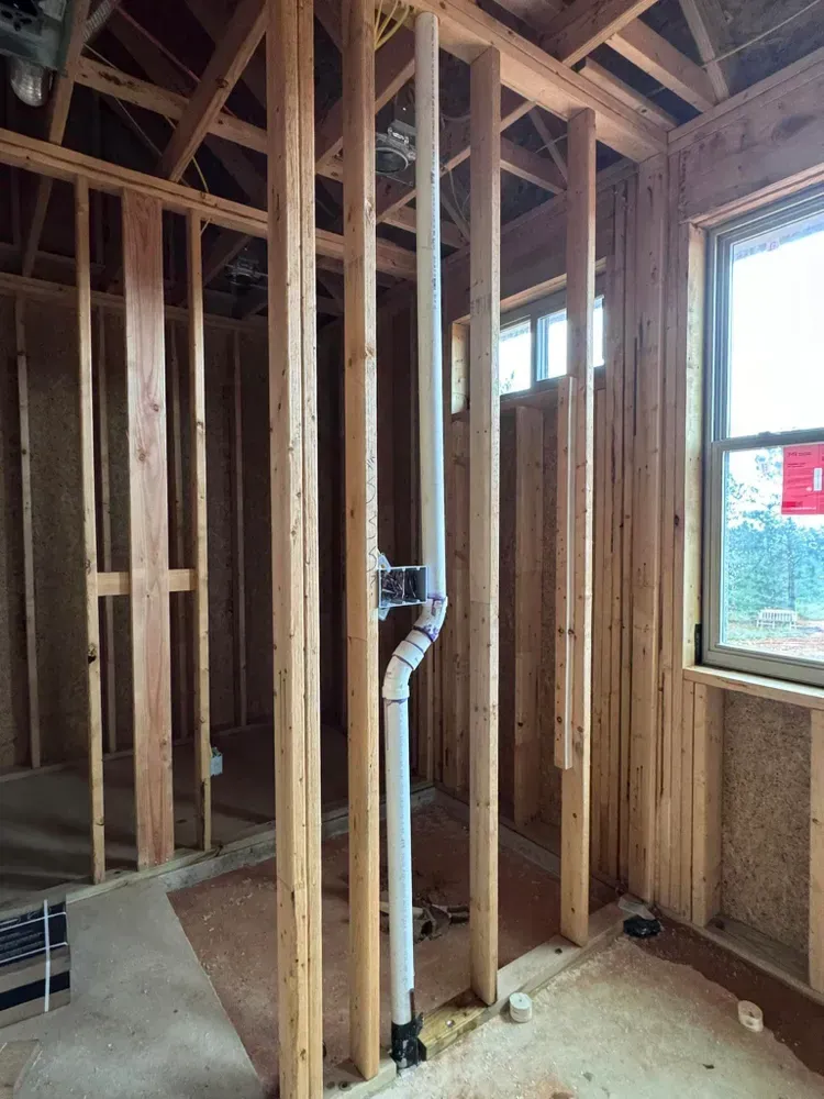 A room in a house under construction with wooden beams and pipes.