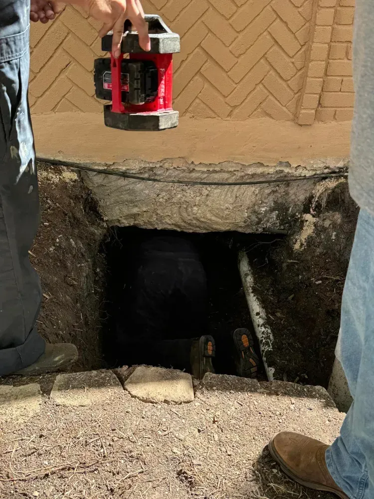 A man is standing in a hole holding a red tool.