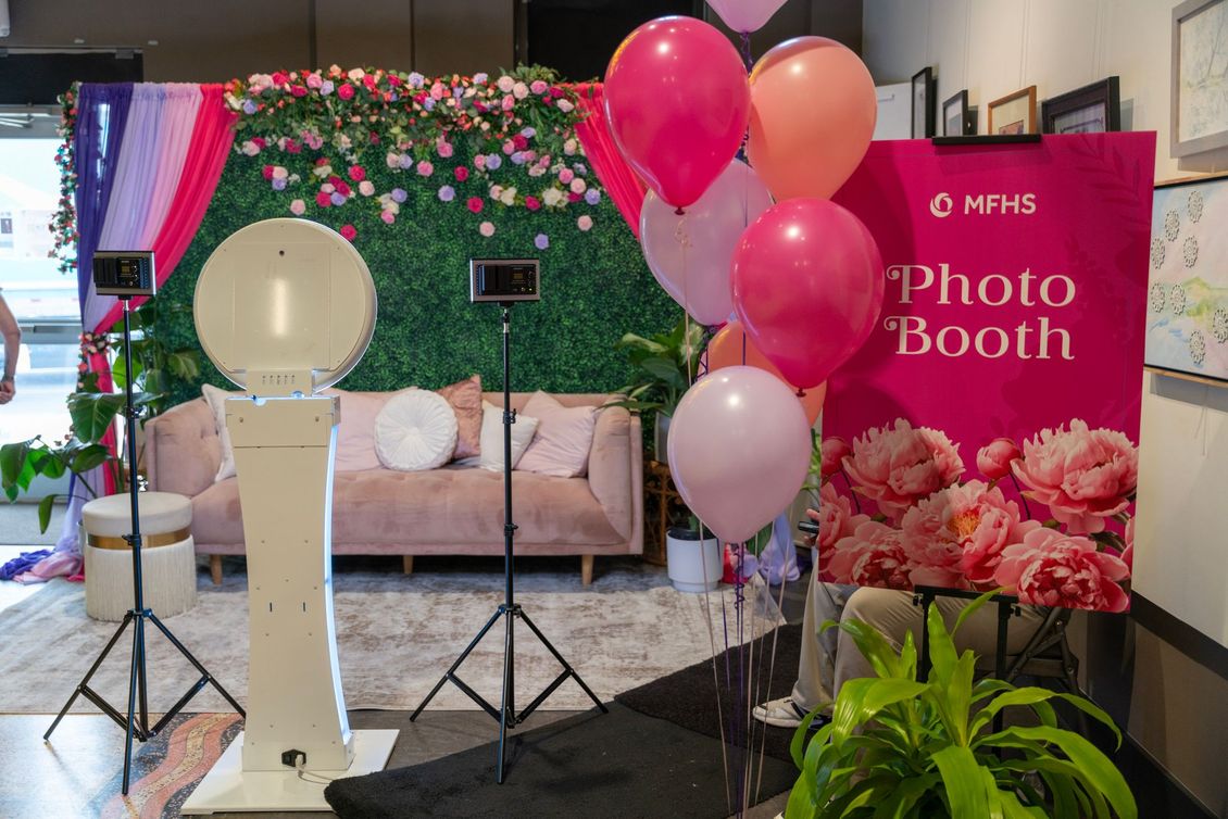 Photo booth setup with pink balloons, floral backdrop, ring light, and photo booth sign in a decorated room