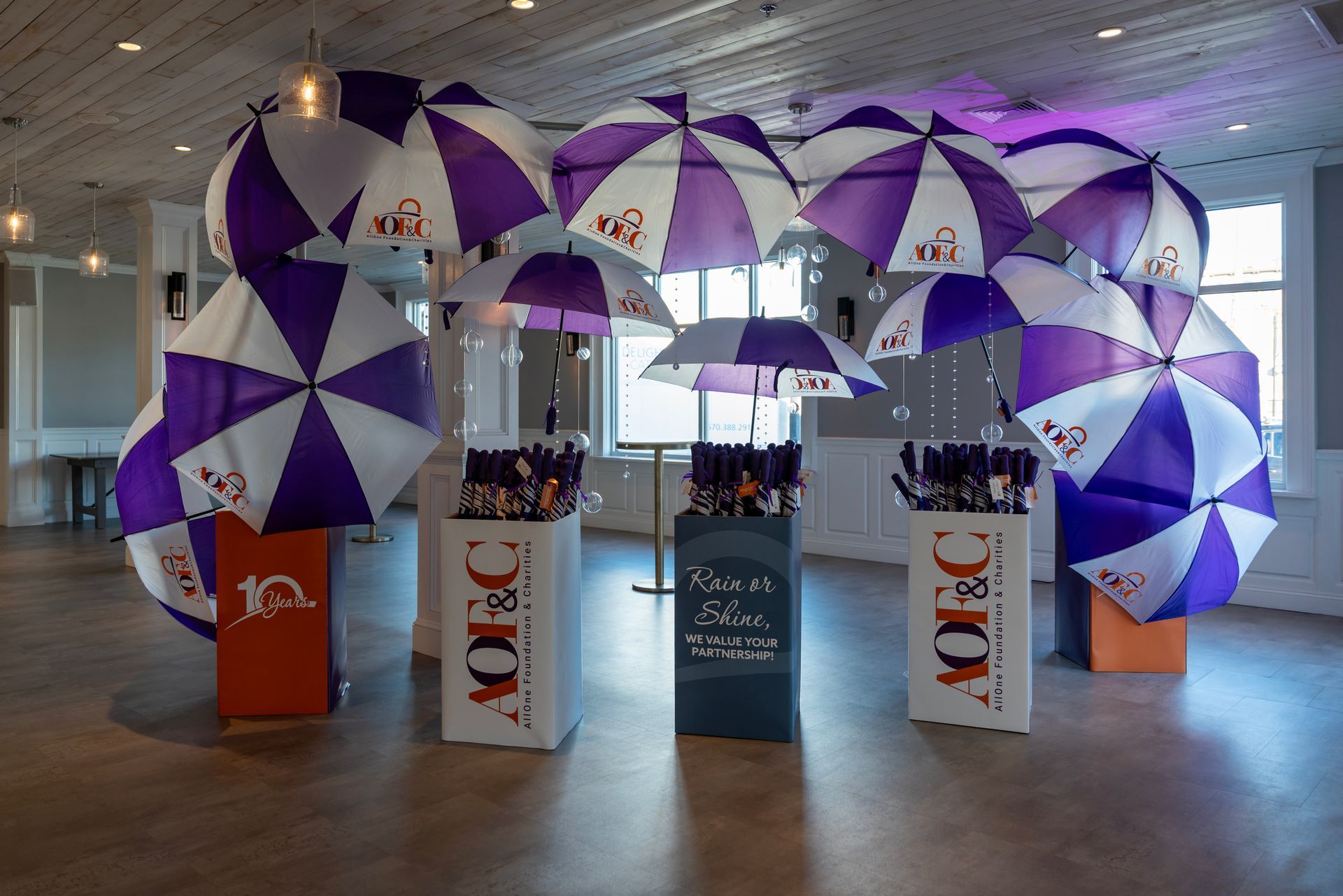 Purple-and-white umbrellas hanging over branded display pedestals in a spacious indoor venue
