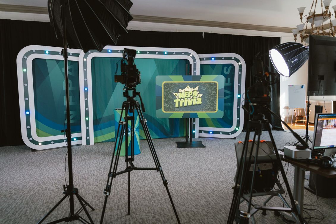 Studio set with cameras and lights facing a teal backdrop and monitor displaying a logo