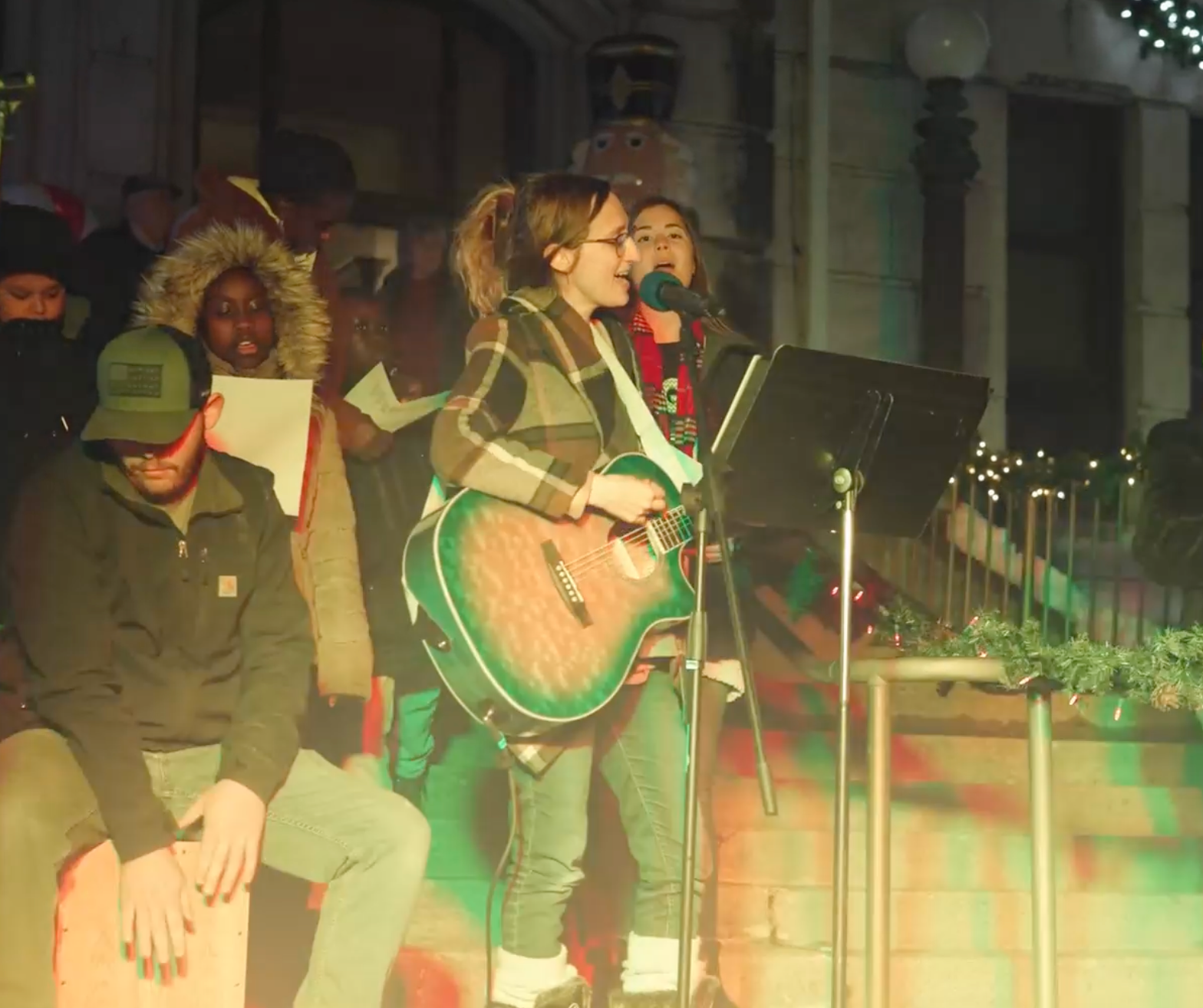 Musicians performing onstage, with a singer playing an acoustic guitar at a microphone.