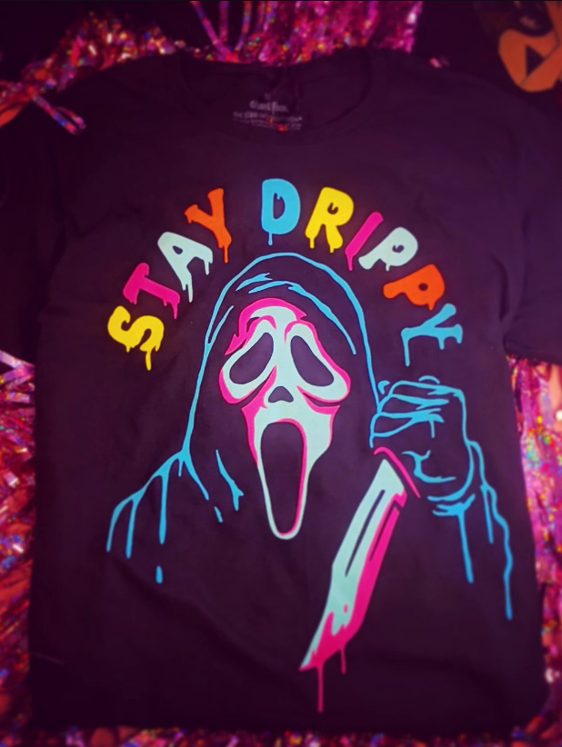 A black t-shirt with a colorful, neon-style illustration of the Ghostface mask holding a knife and the text 